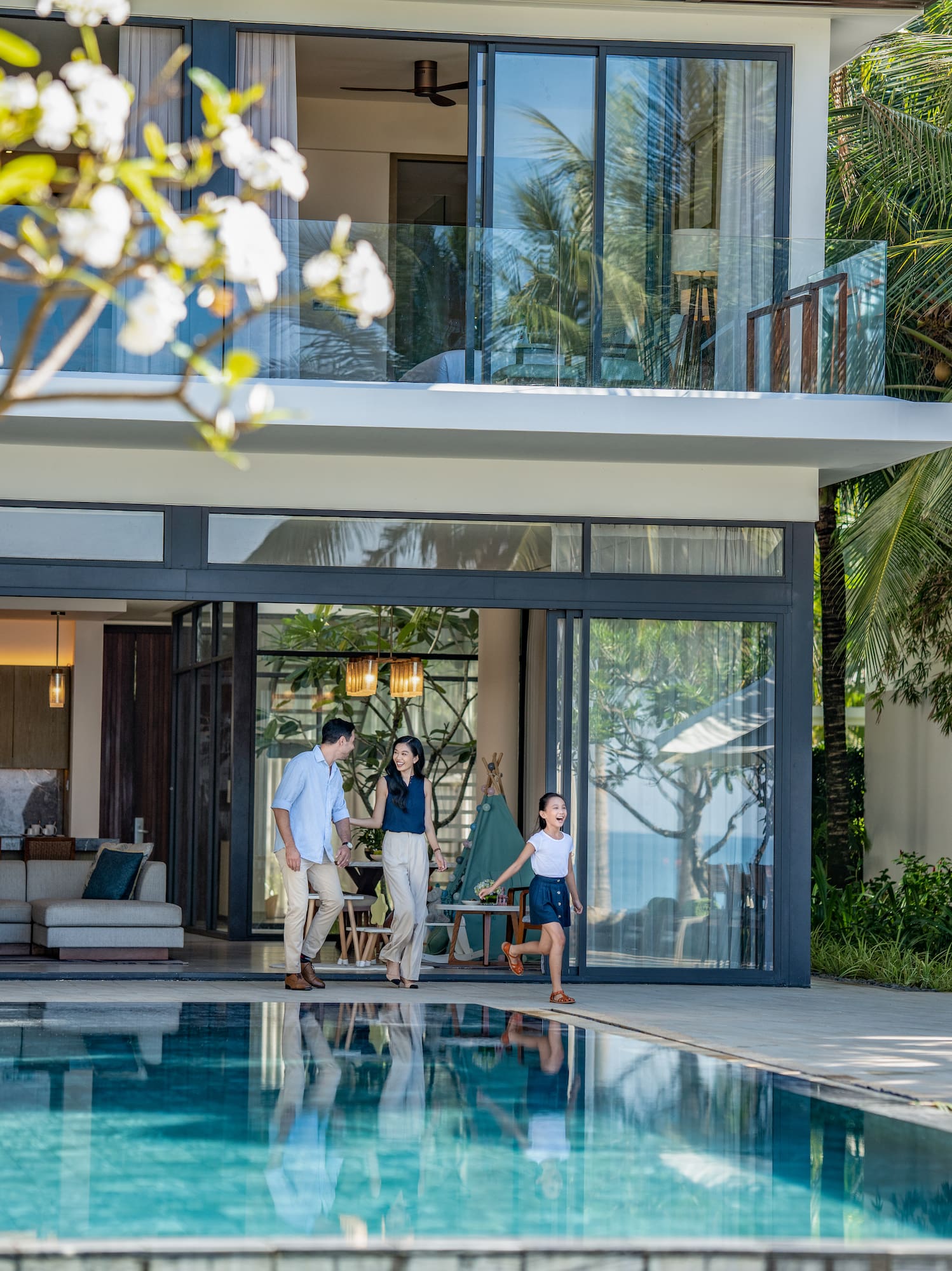 Family walking from luxury tropical villa to sparkling pool.