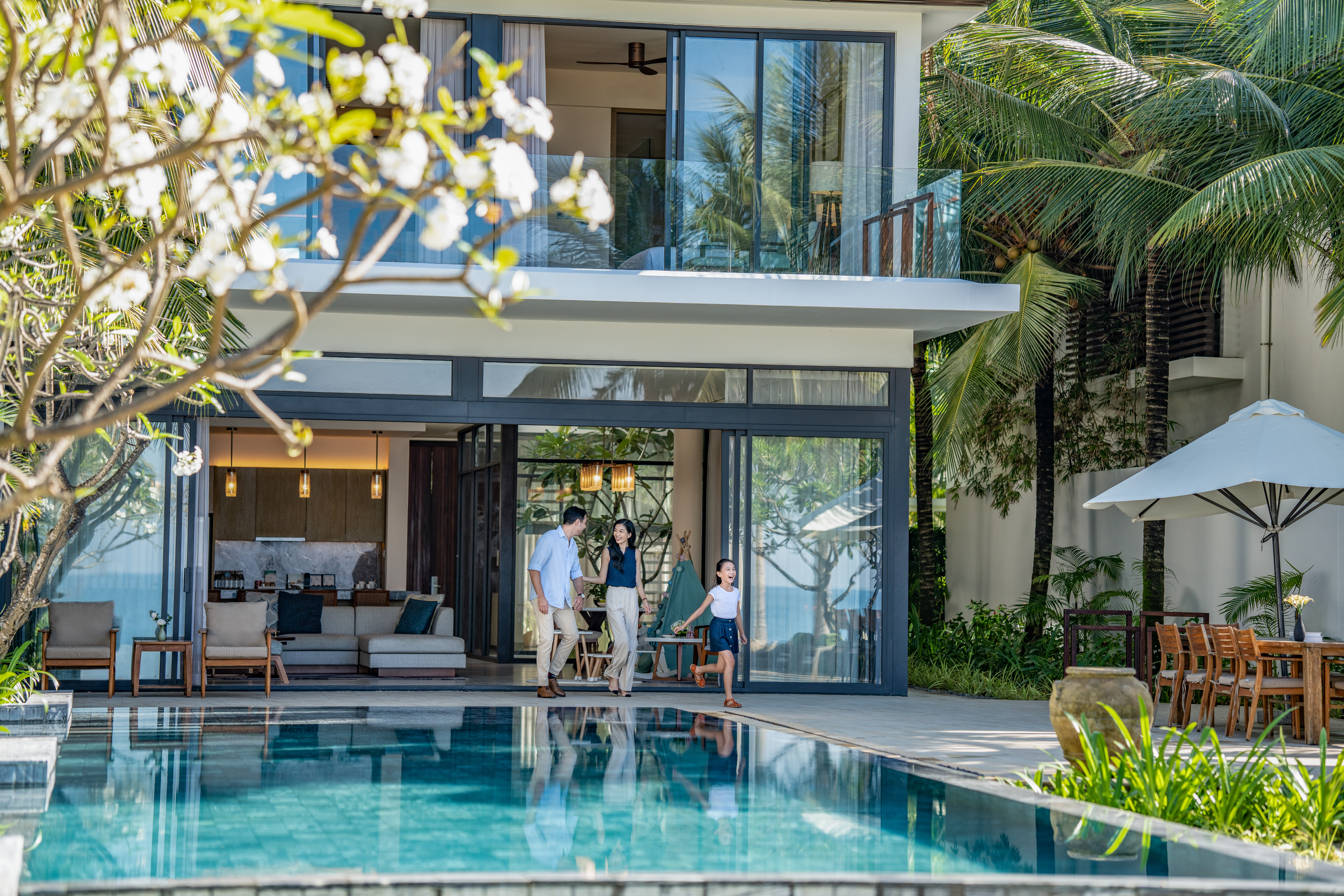 Family walking from luxury tropical villa to sparkling pool.