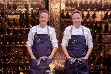 two men wearing aprons standing in front of a wall