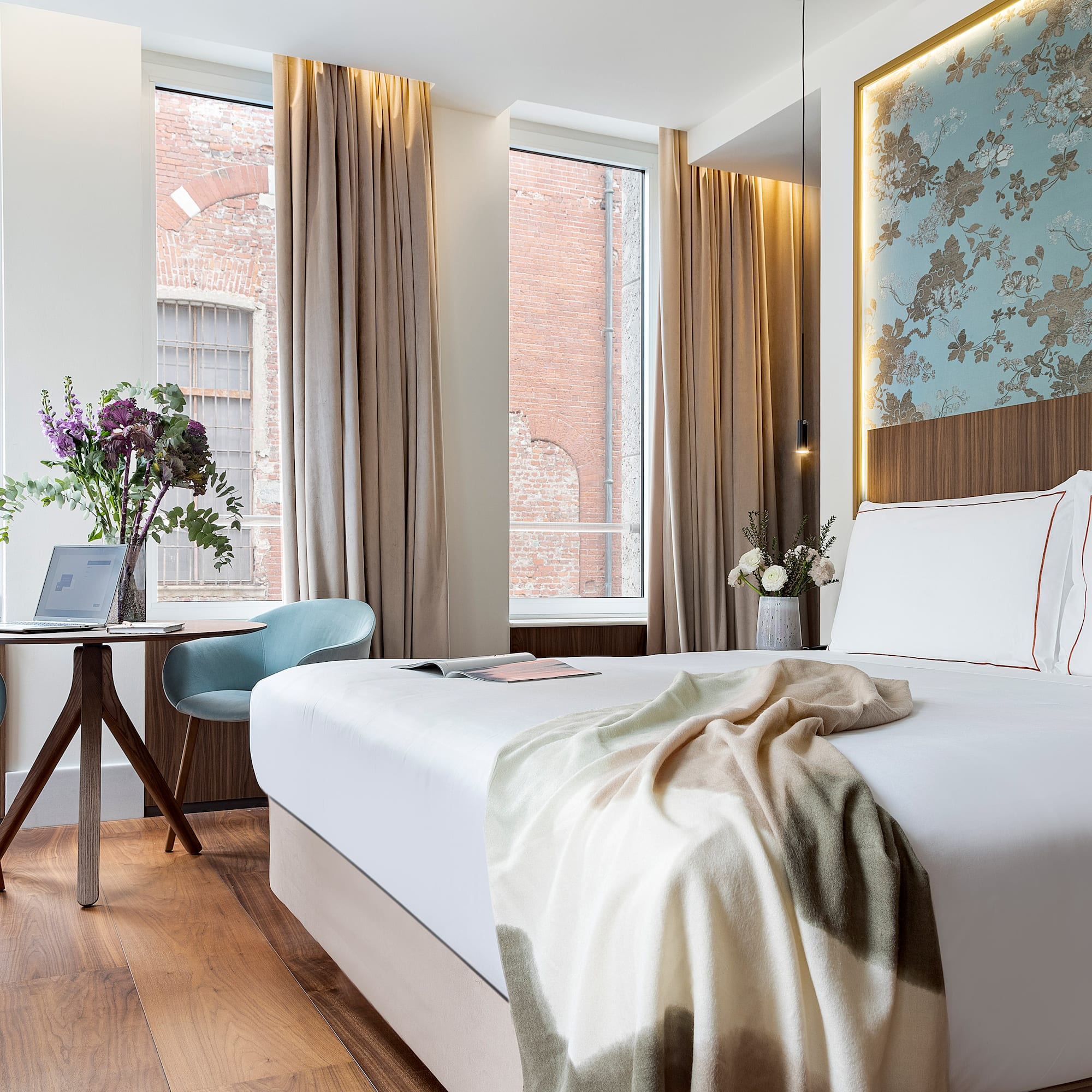 a bed with a blanket and a chair in a room with windows