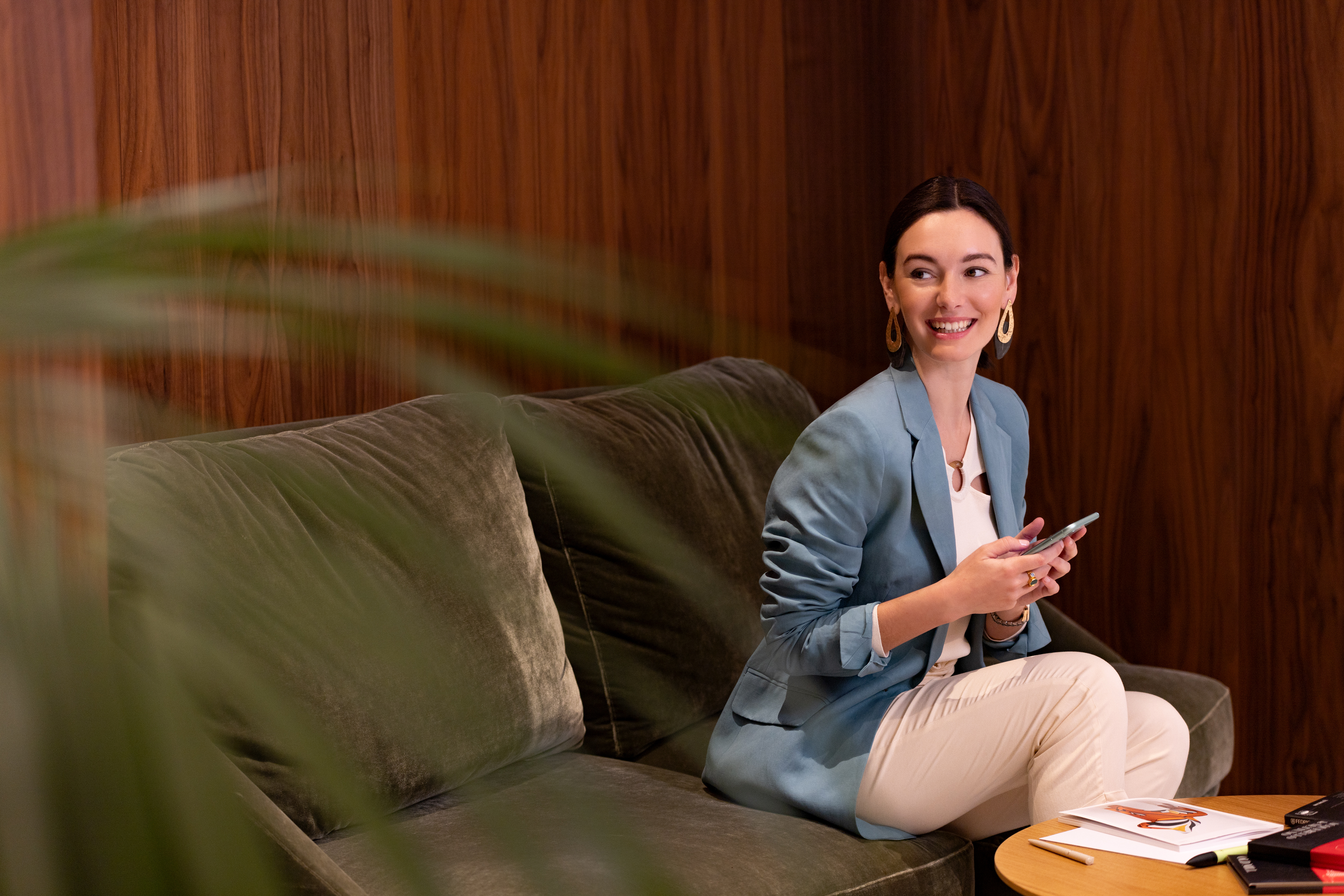 Smiling professional woman using phone on green sofa in modern lounge.