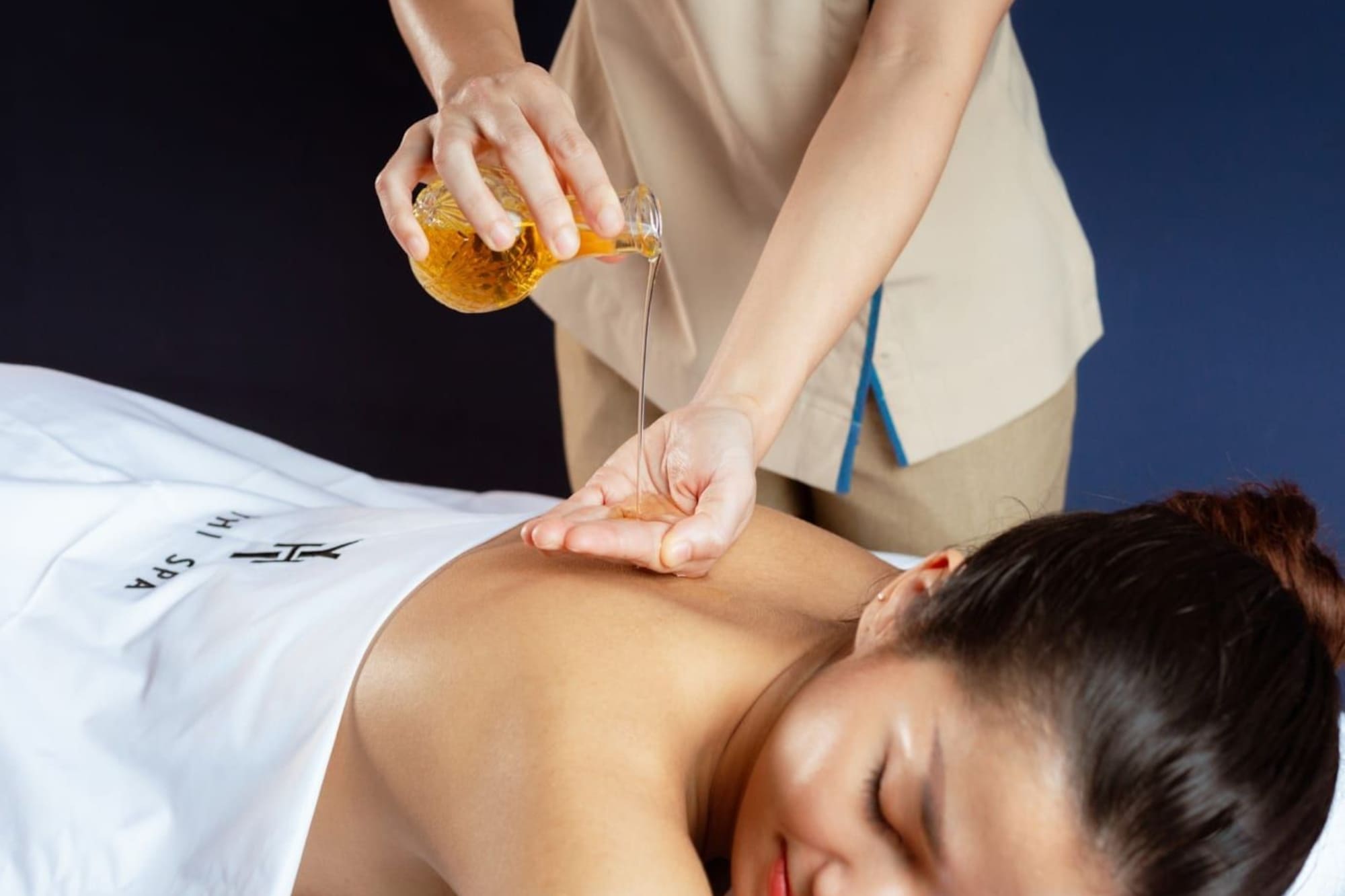Therapist pouring massage oil onto client's hand for a spa treatment.