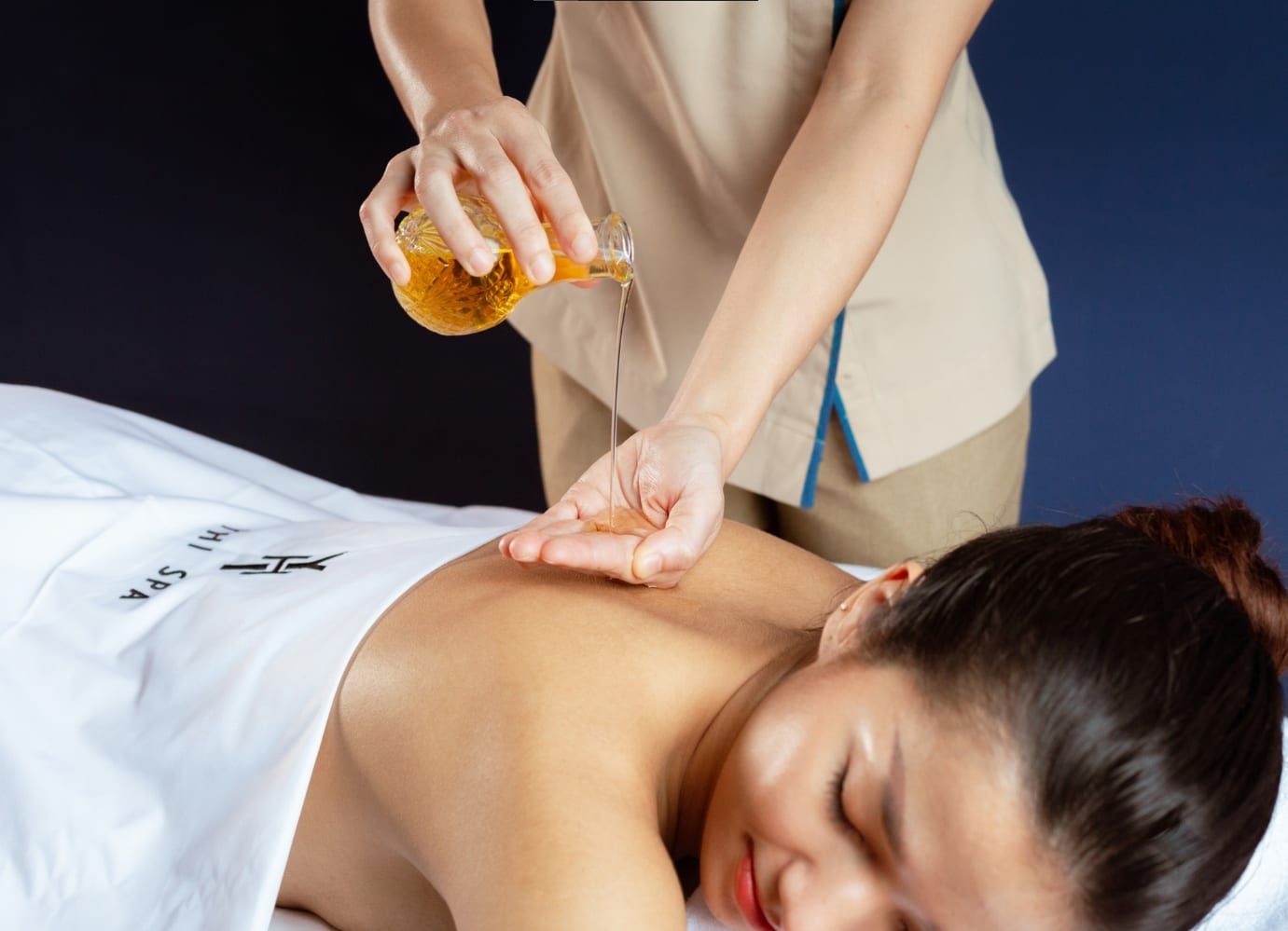 Therapist pouring massage oil onto client's hand for a spa treatment.