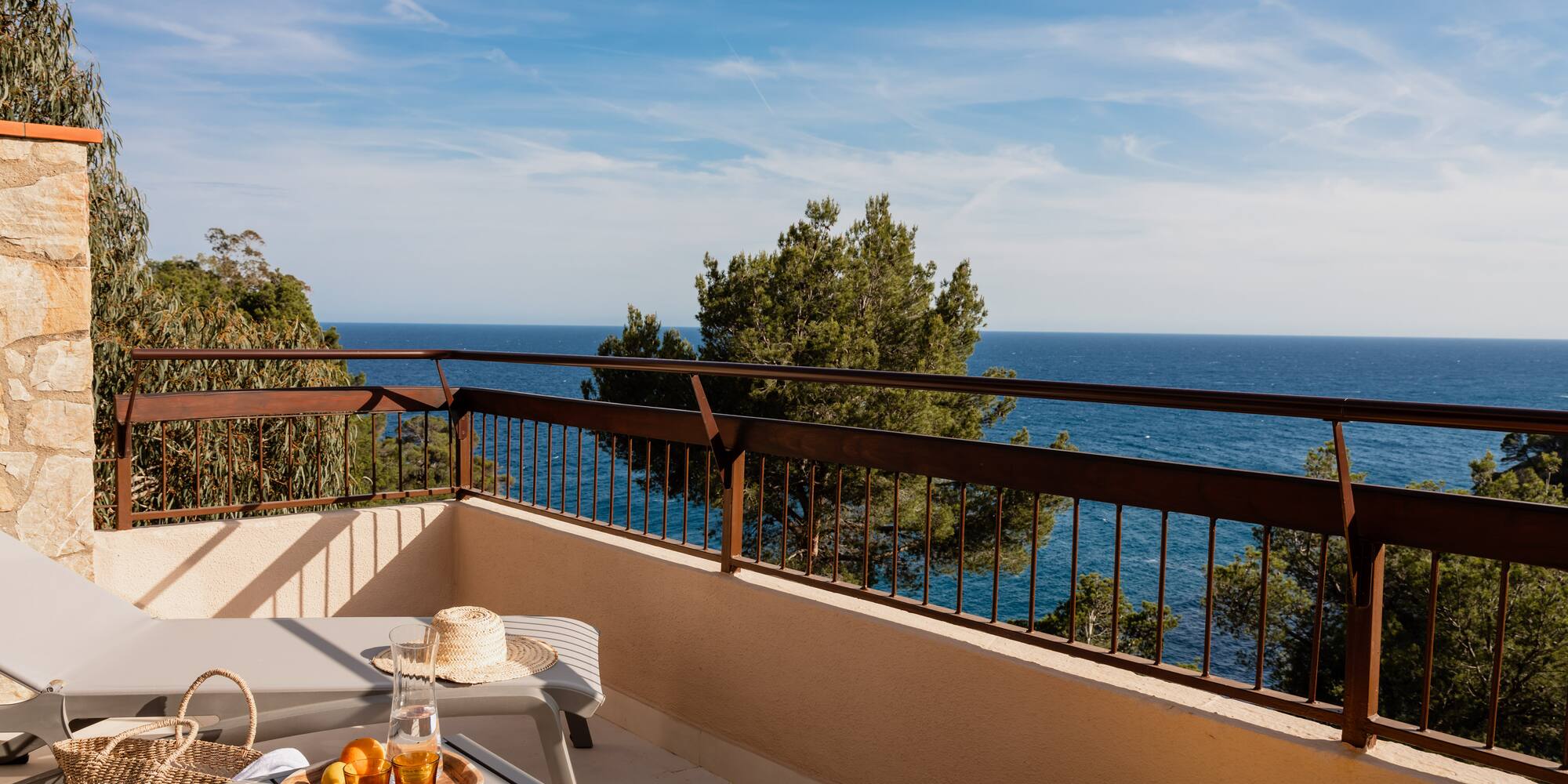 Hotel balcony with lounge chairs, refreshing drinks, fruit, and scenic ocean view.