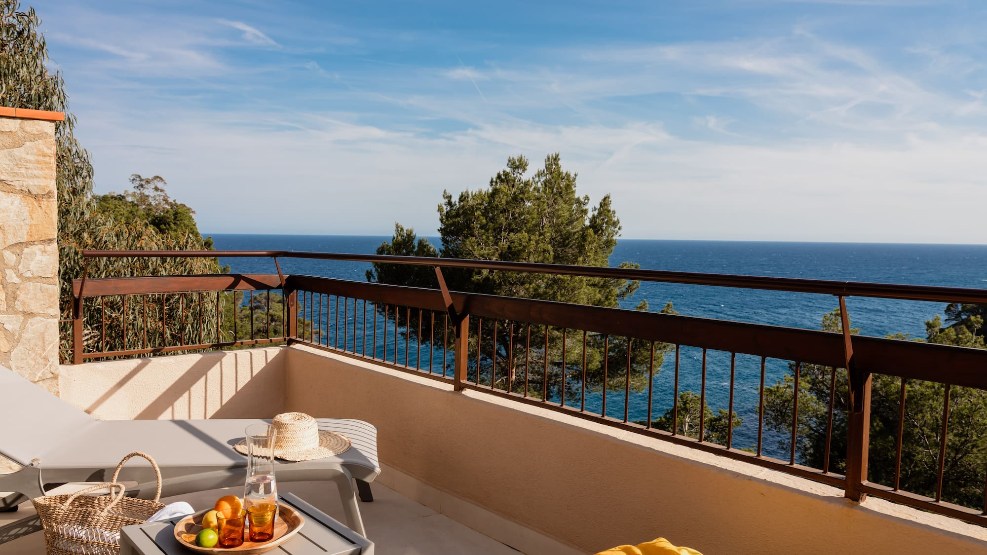 Hotel balcony with lounge chairs, refreshing drinks, fruit, and scenic ocean view.