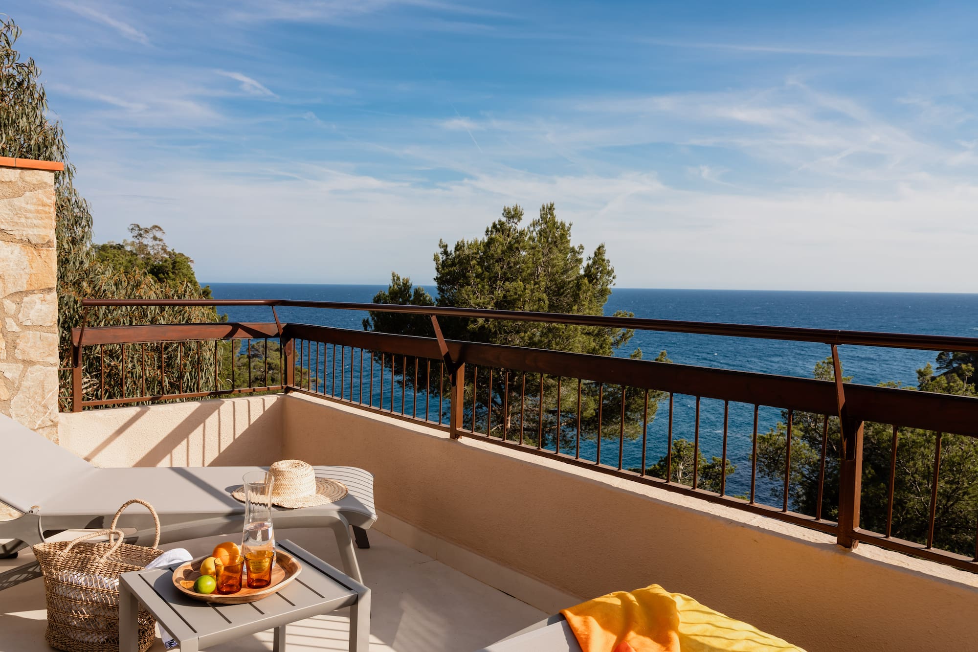 Hotel balcony with lounge chairs, refreshing drinks, fruit, and scenic ocean view.