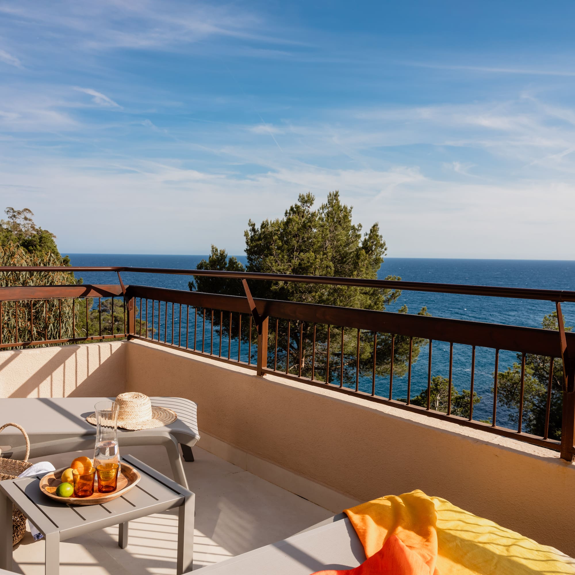 Hotel balcony with lounge chairs, refreshing drinks, fruit, and scenic ocean view.