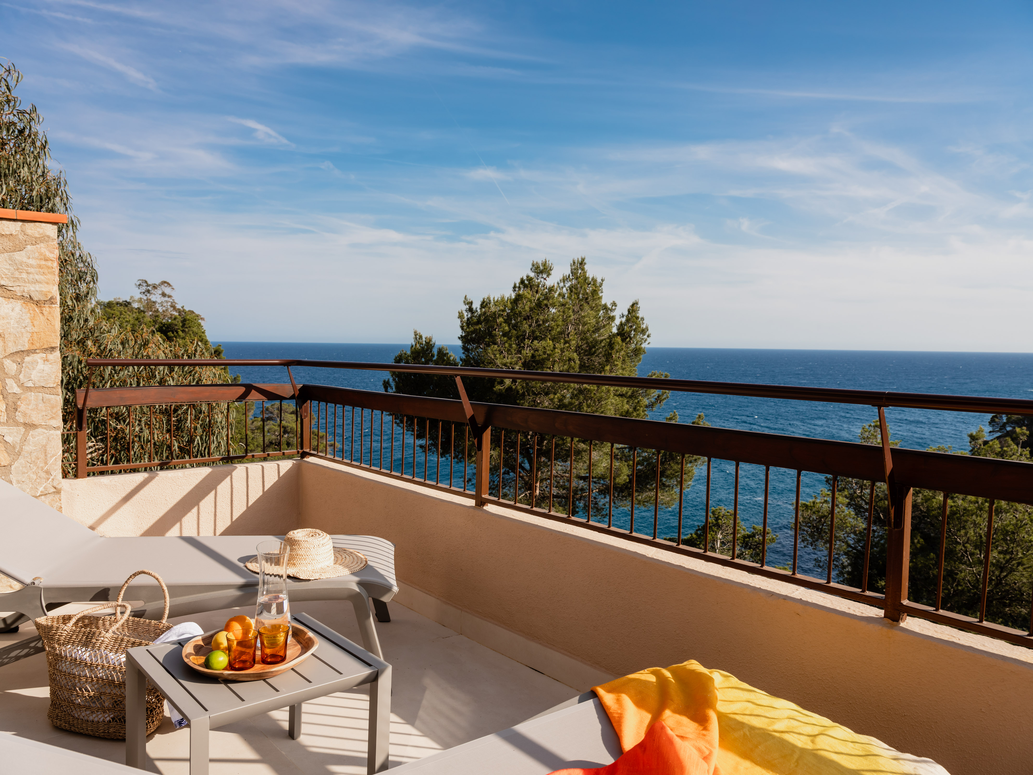 Hotel balcony with lounge chairs, refreshing drinks, fruit, and scenic ocean view.