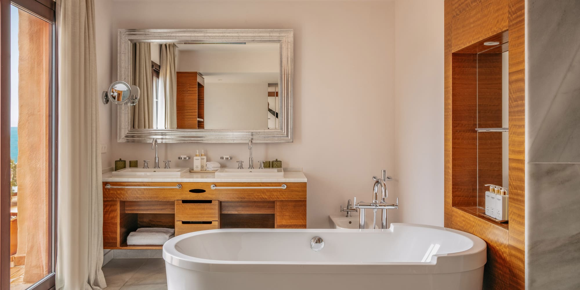 Luxury bathroom with freestanding tub, double vanity, and balcony with sea view.