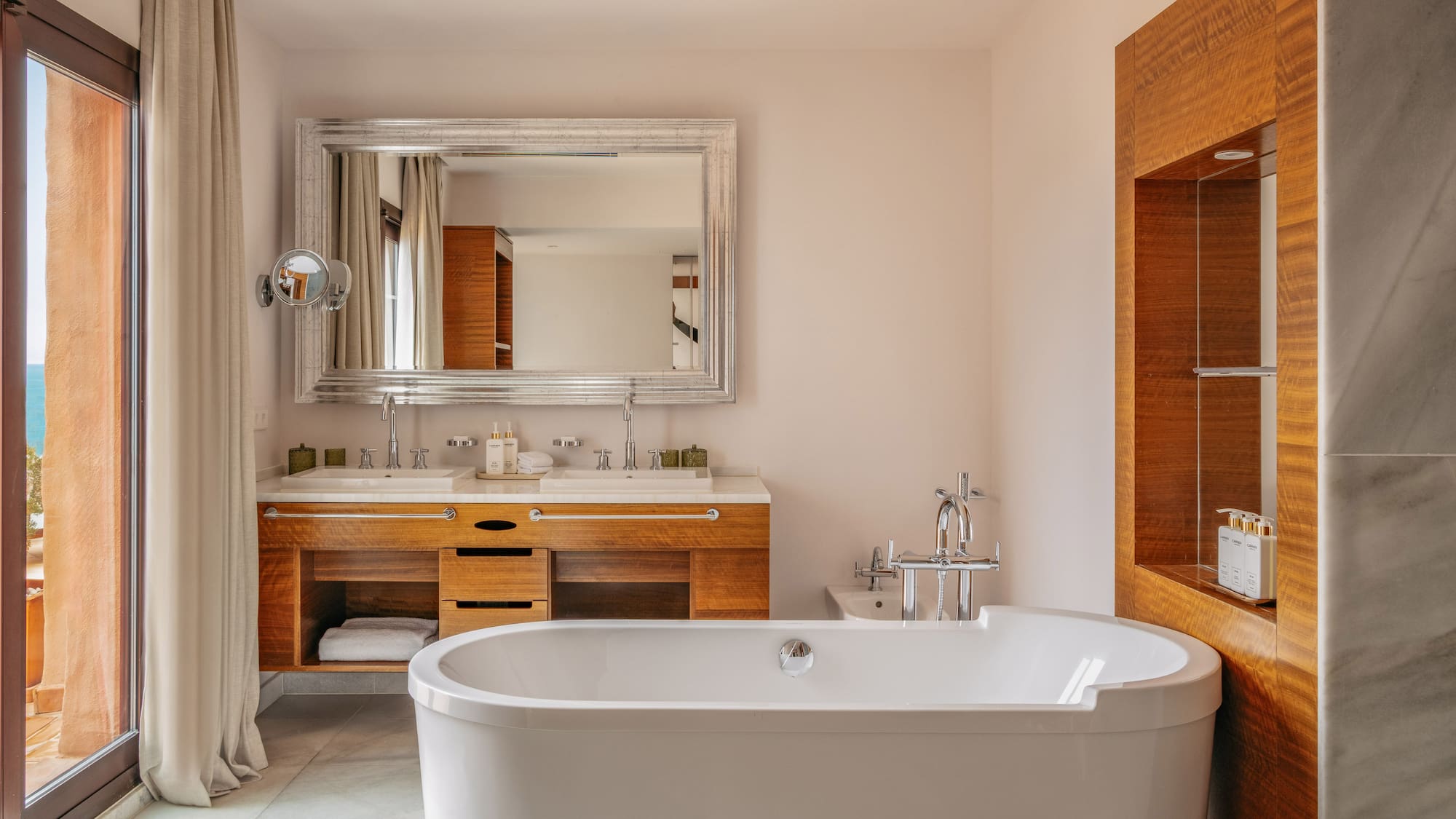 Luxury bathroom with freestanding tub, double vanity, and balcony with sea view.