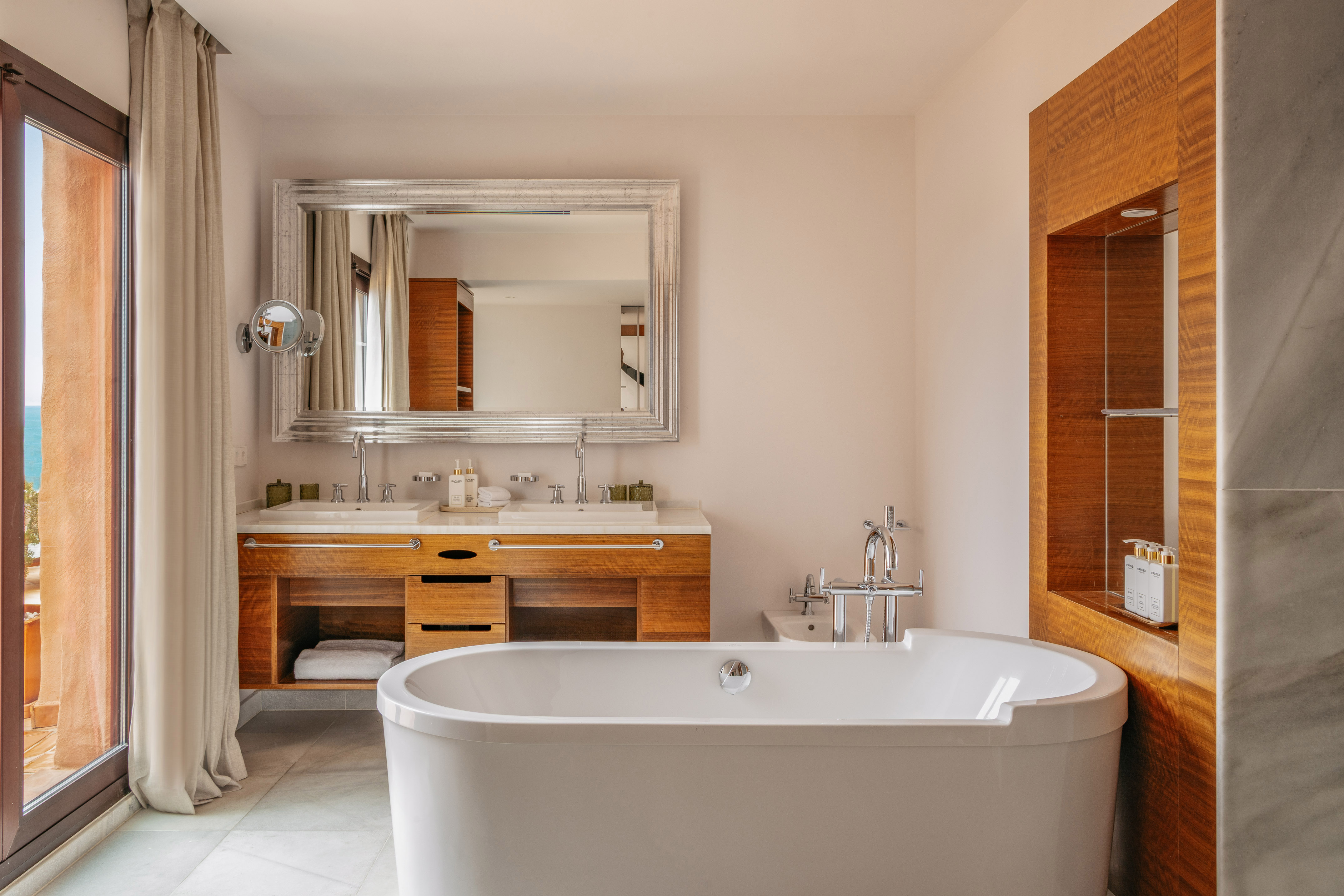 Luxury bathroom with freestanding tub, double vanity, and balcony with sea view.