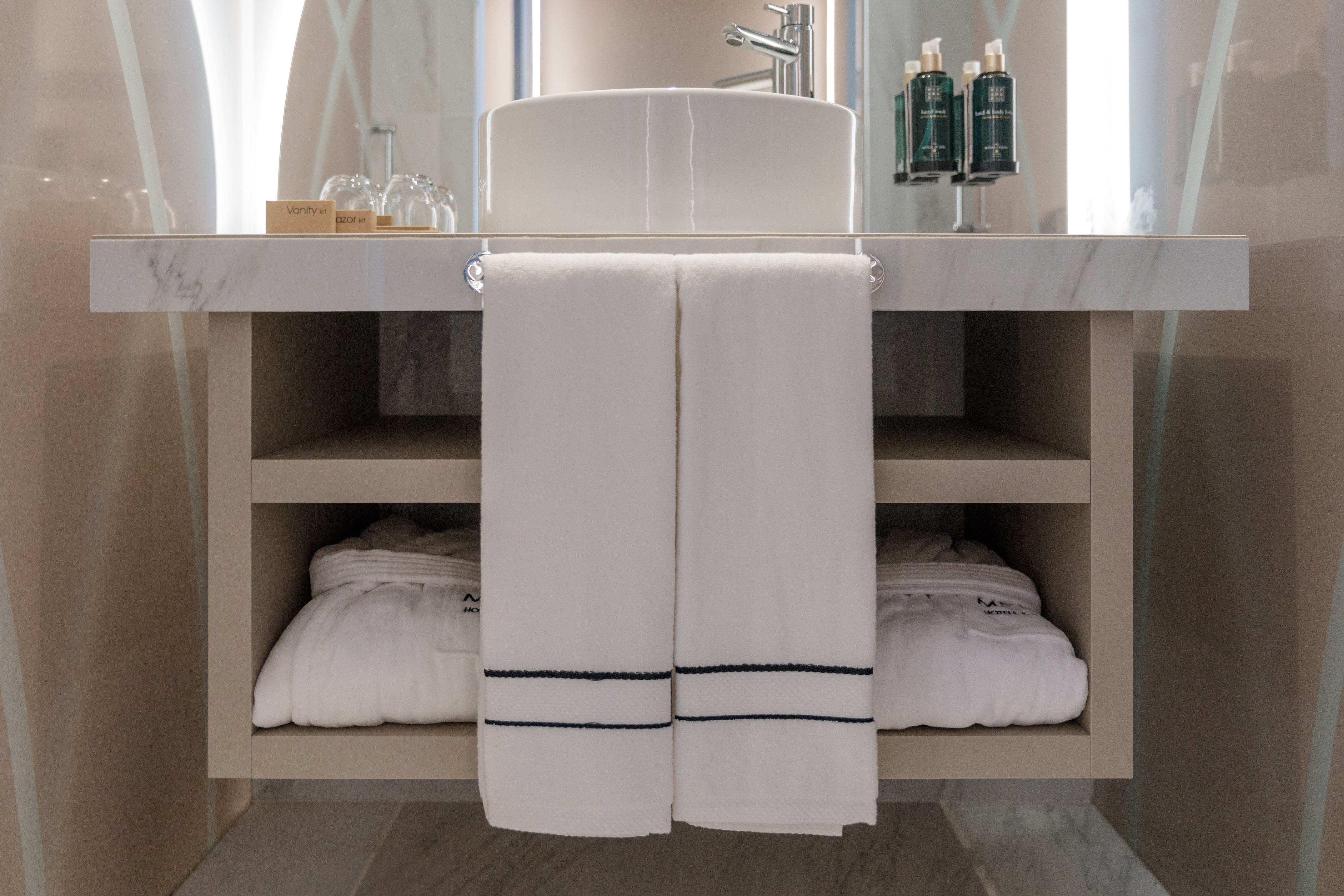 Modern hotel bathroom vanity with vessel sink, white towels, and bathrobes.