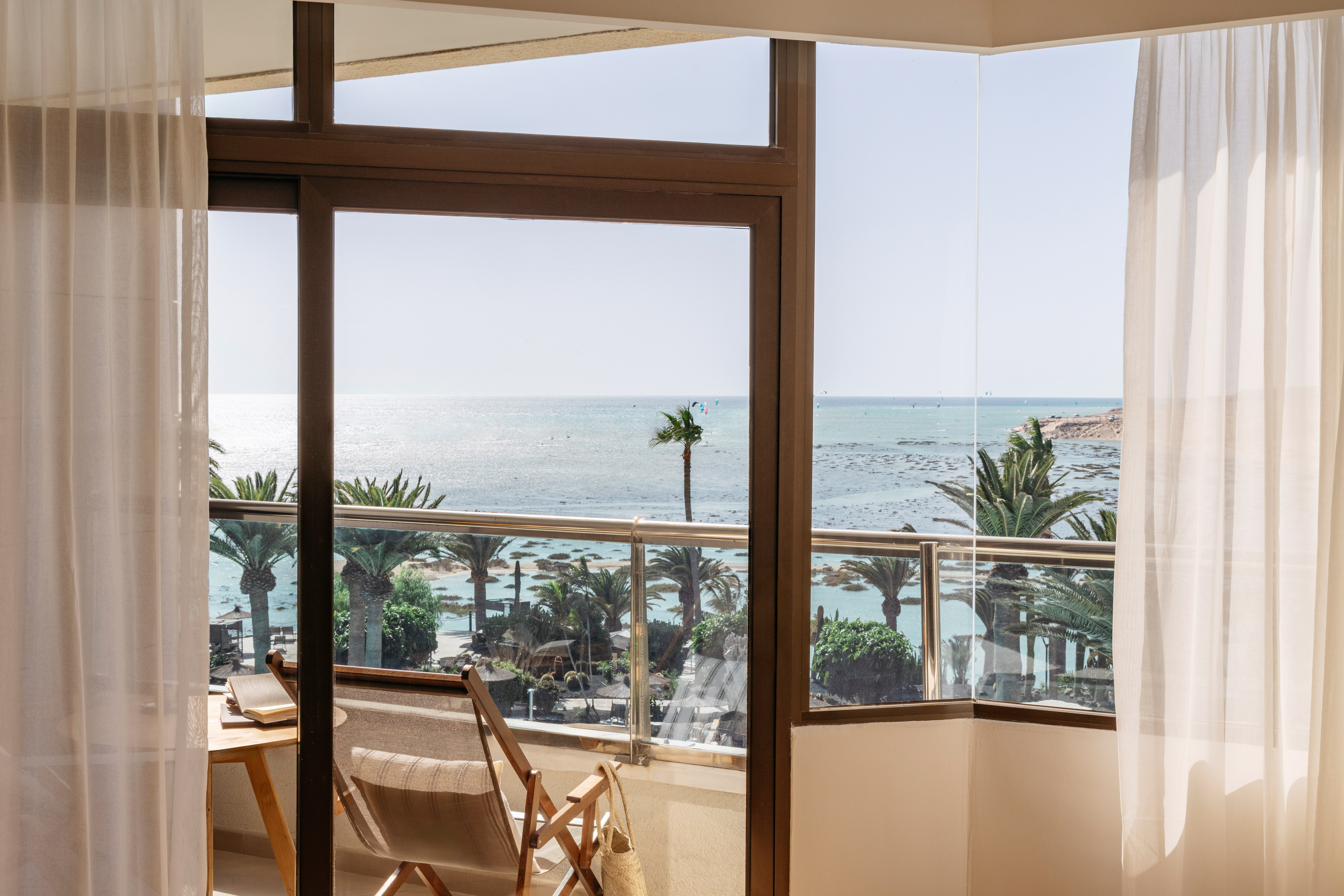 Sunny hotel balcony with ocean view, palm trees, and a clear blue sea.