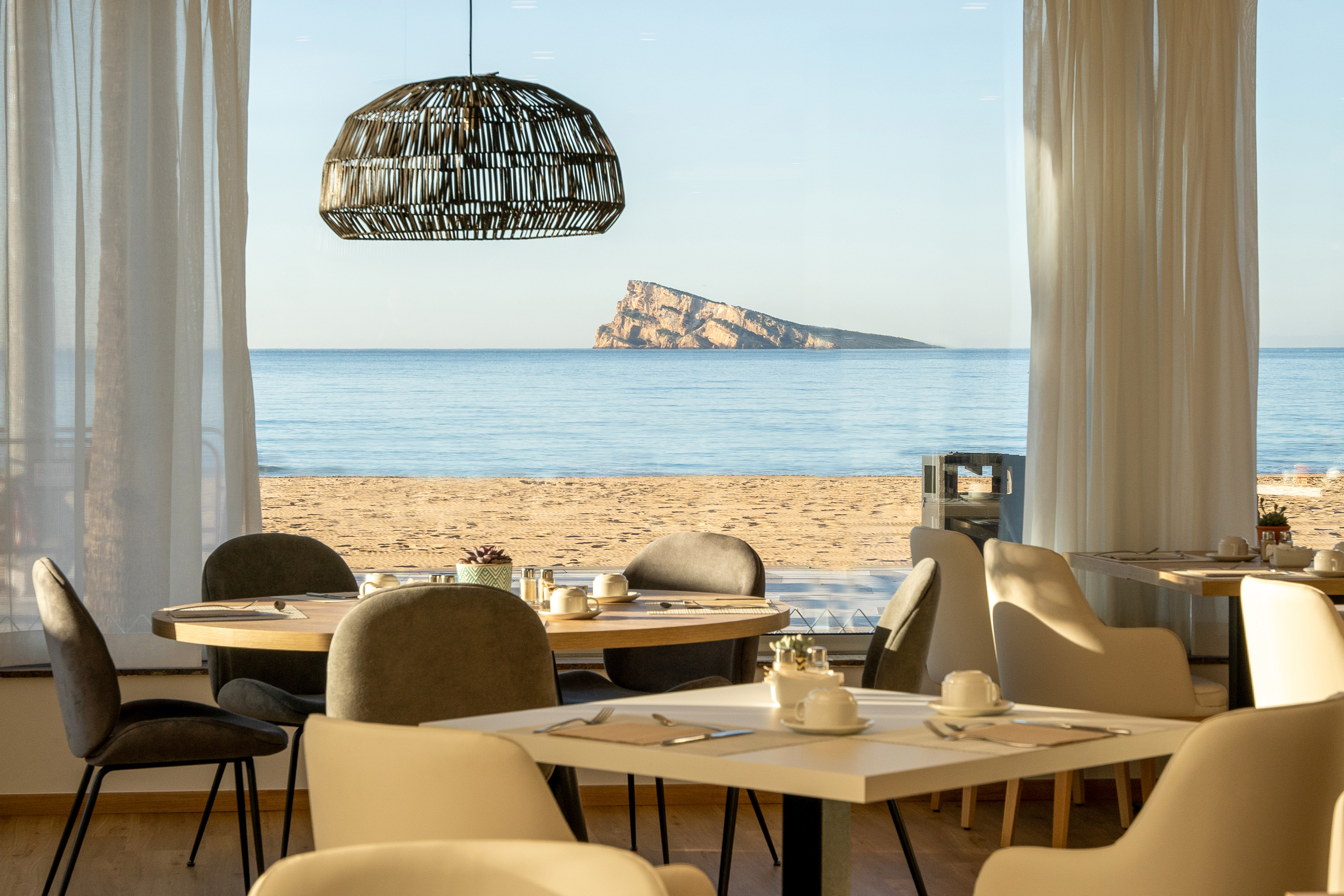Coastal dining area with sea view, sandy beach, and distant rocky island.