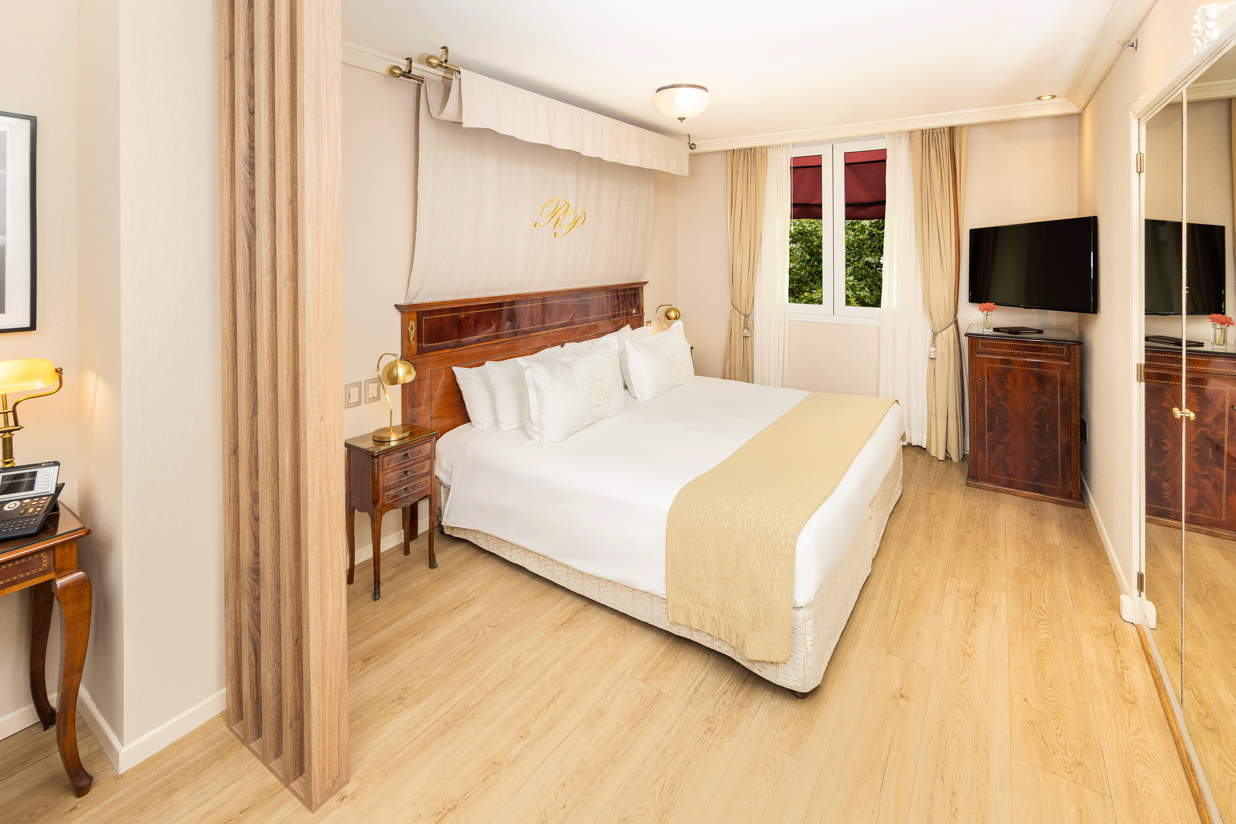 Luxury hotel room with classic wood furniture, white bed, and natural light.