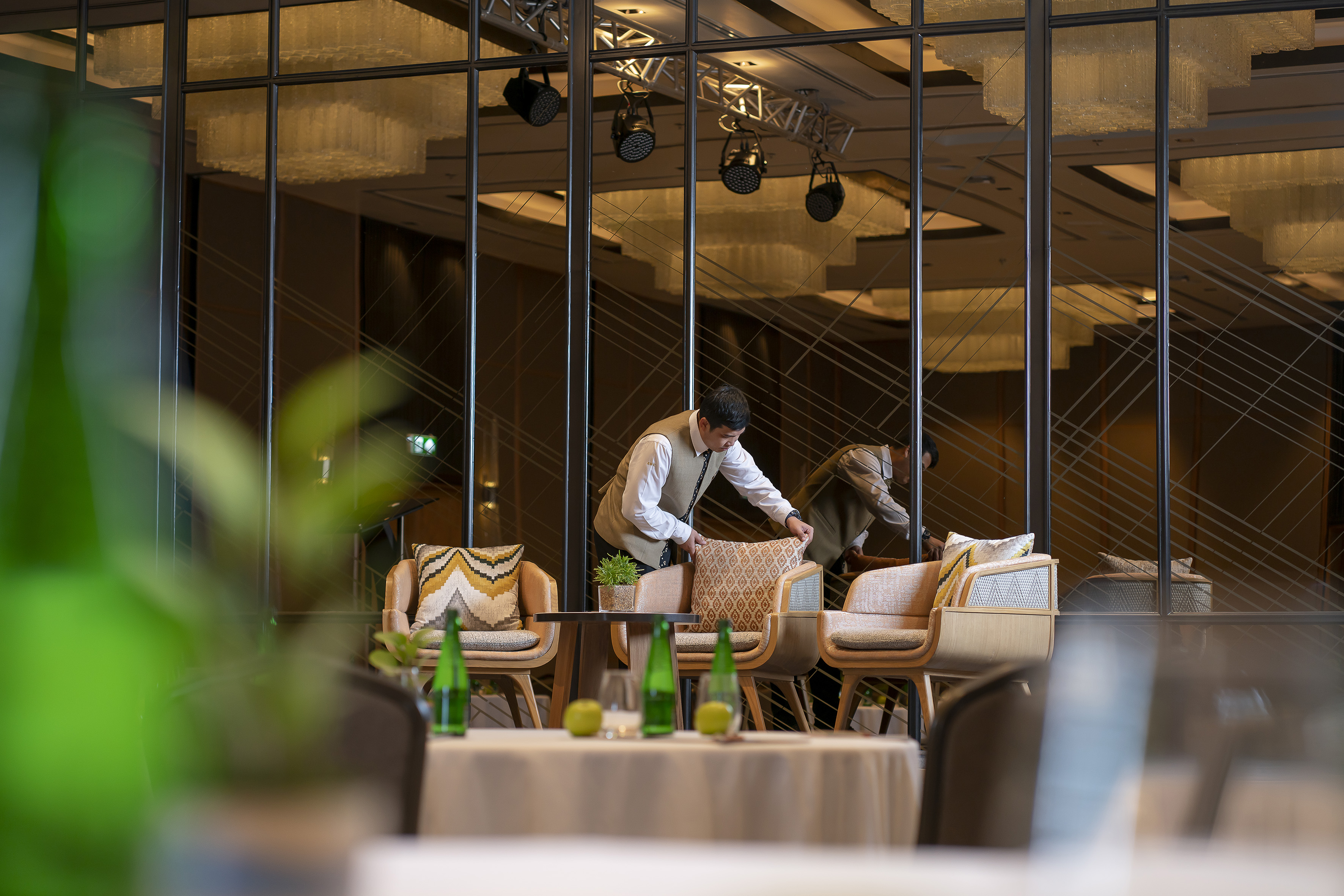 Hotel staff arranging modern lounge chairs in a stylish restaurant setting.