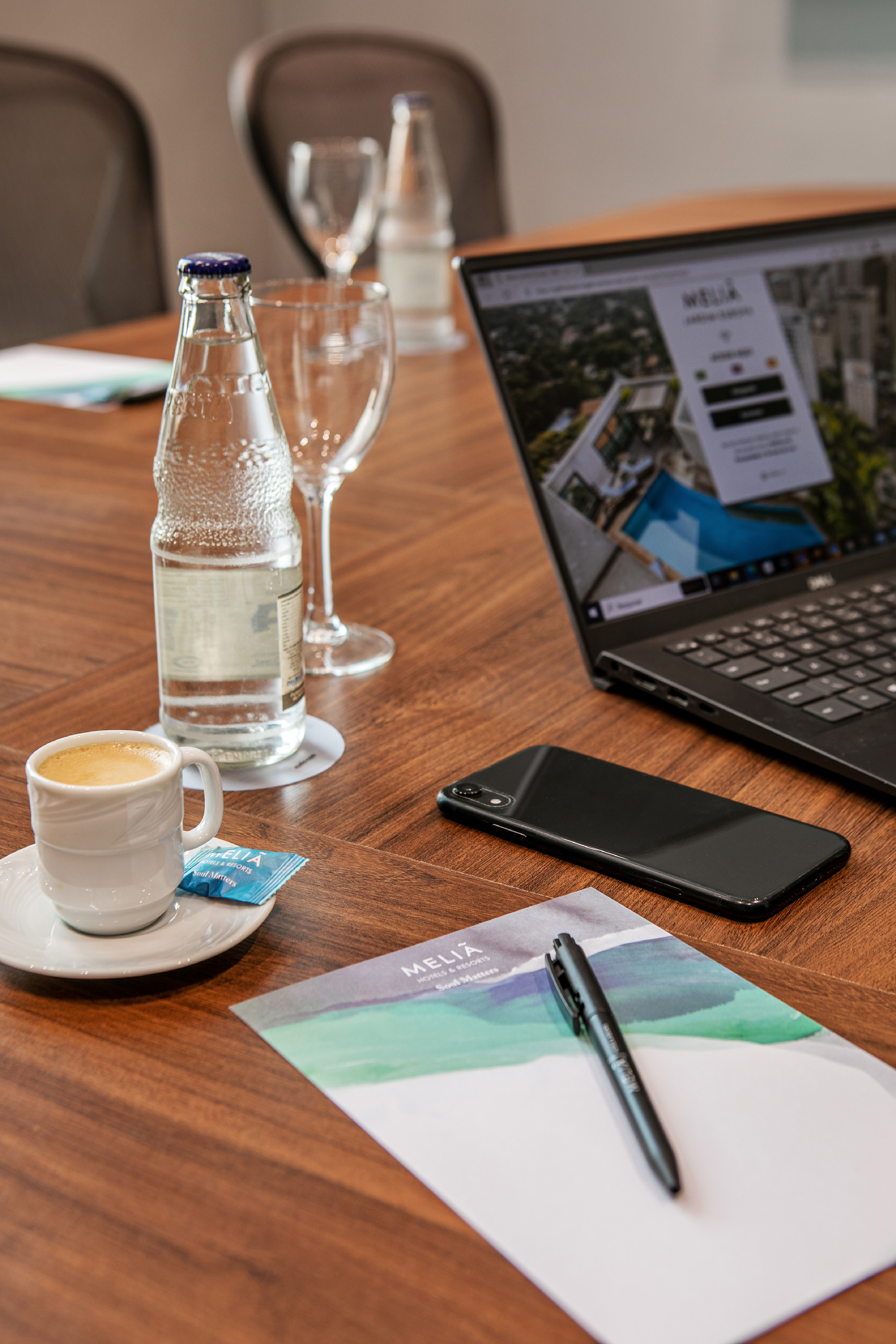 Meliá Hotels laptop, coffee, water, phone, notepad on a wooden table.
