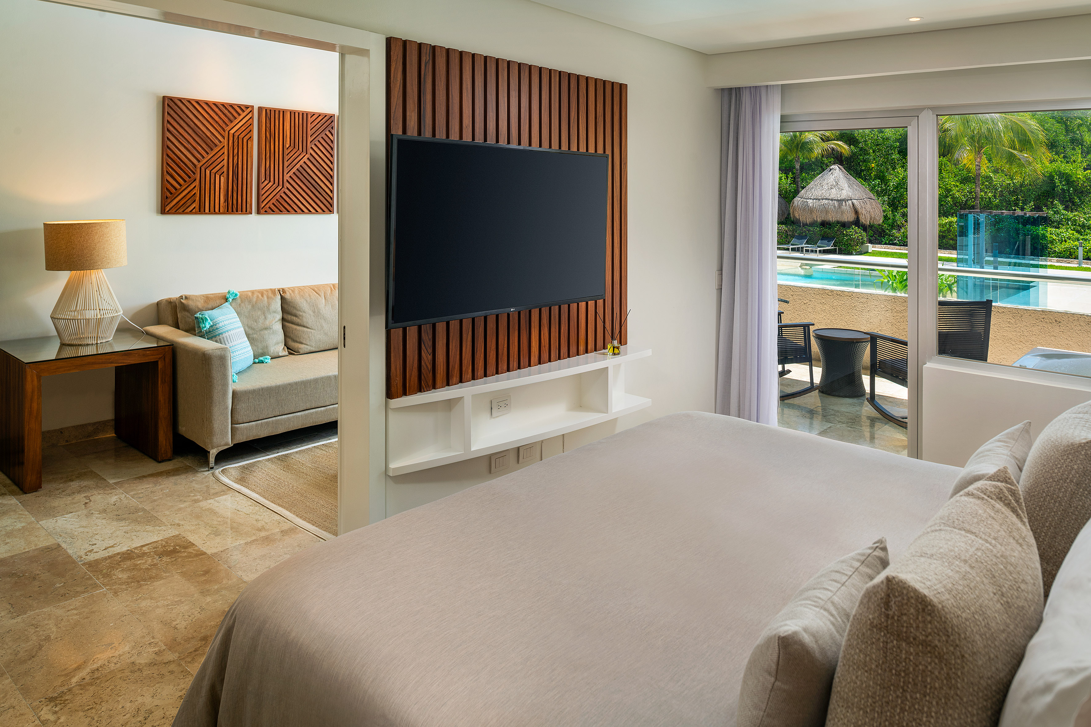 Modern bedroom suite with pool view, wood TV wall, and comfortable living area.