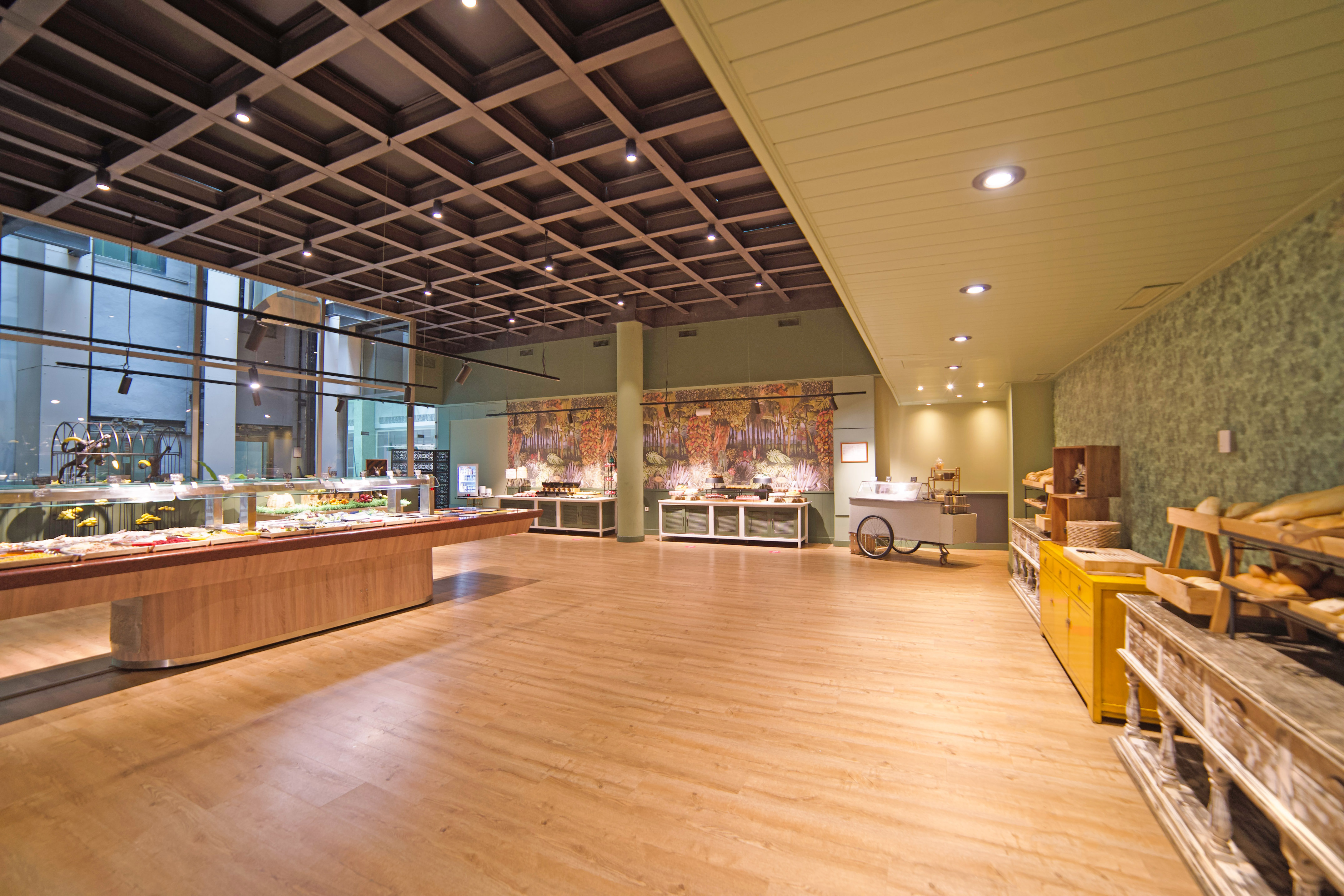 Spacious hotel buffet restaurant with food displays, wooden floor, and nature-themed murals.