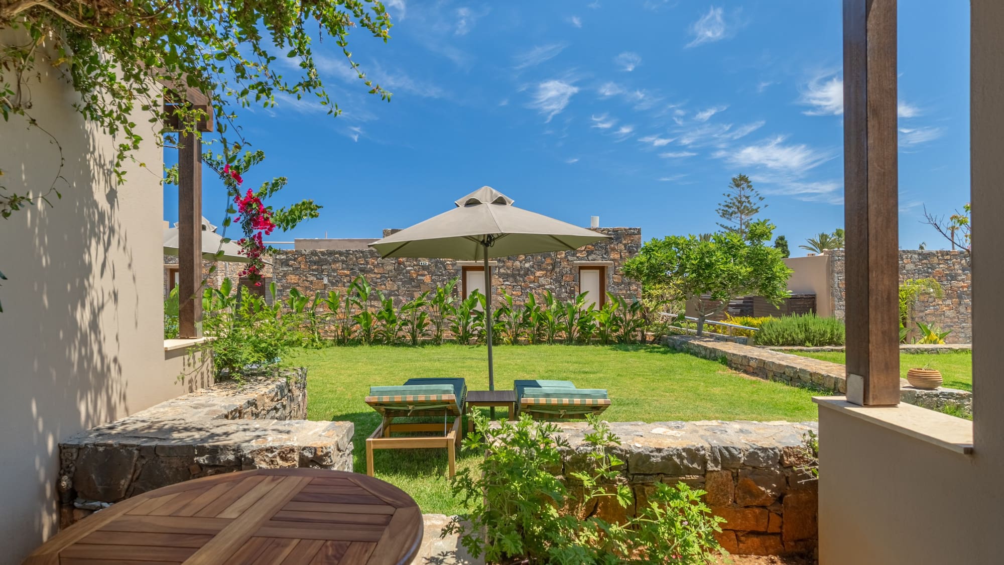 Sunny resort garden patio with loungers, parasol, and stone buildings.