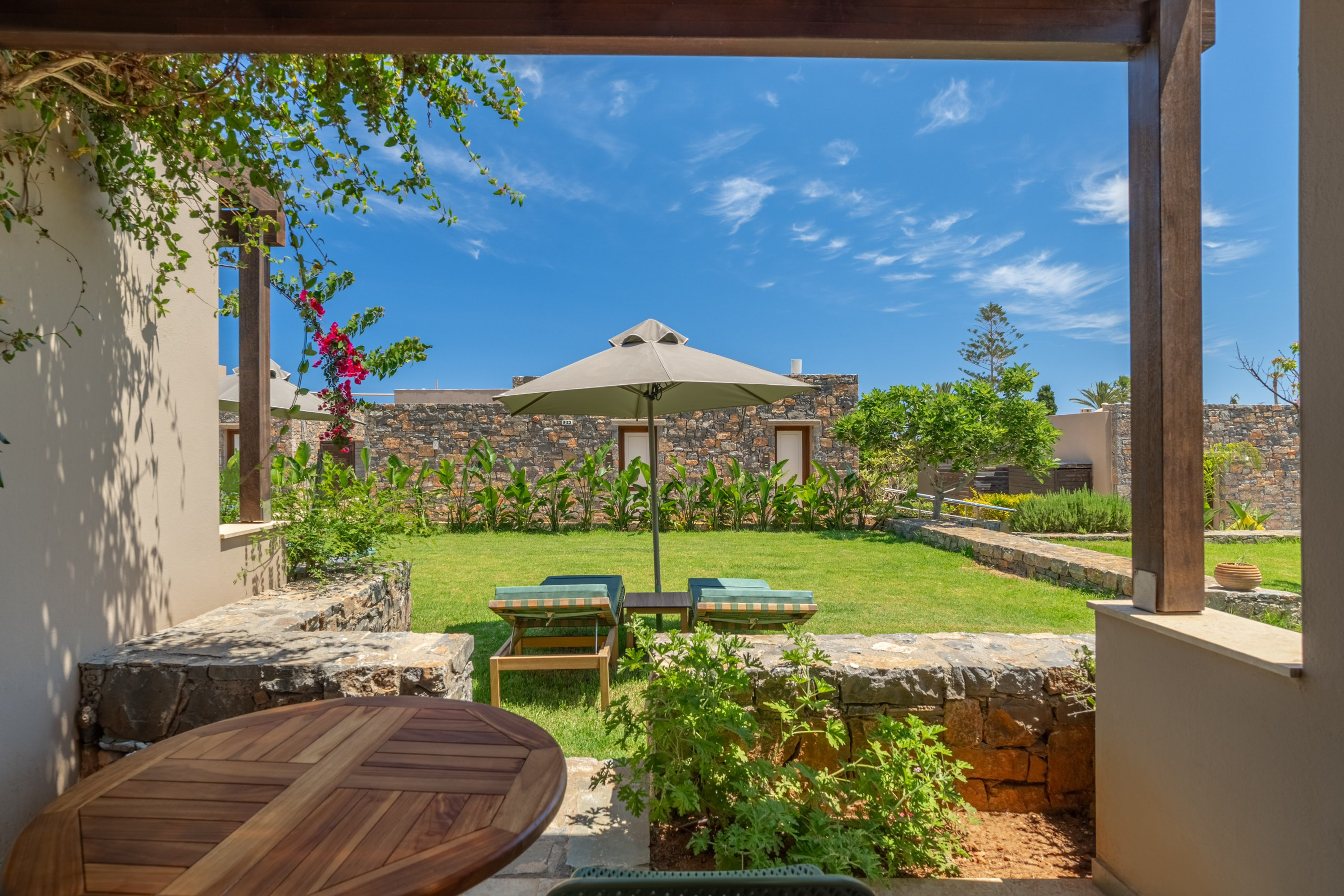 Sunny resort garden patio with loungers, parasol, and stone buildings.
