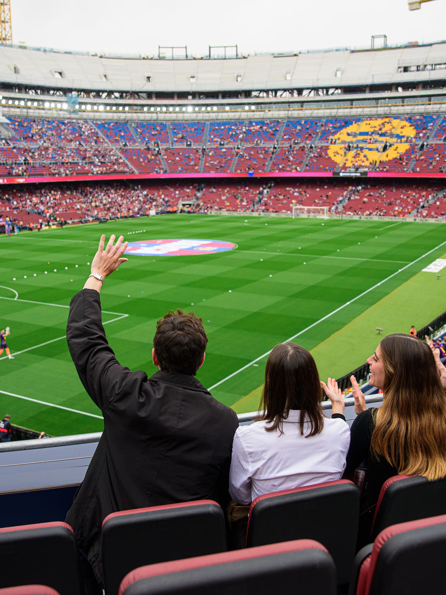 Four fans cheering in a stadium, watching a football match from seats.