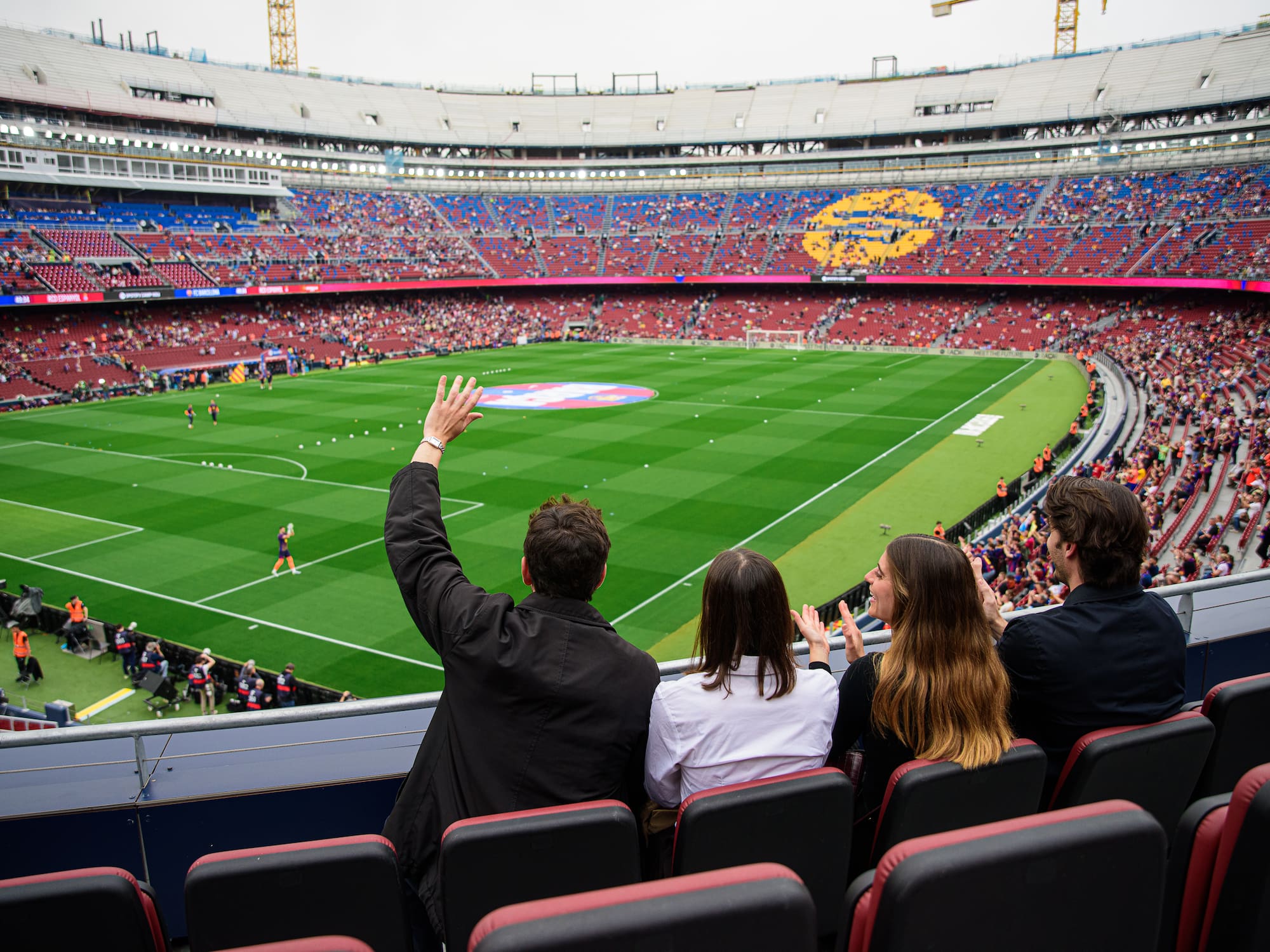 Four fans cheering in a stadium, watching a football match from seats.