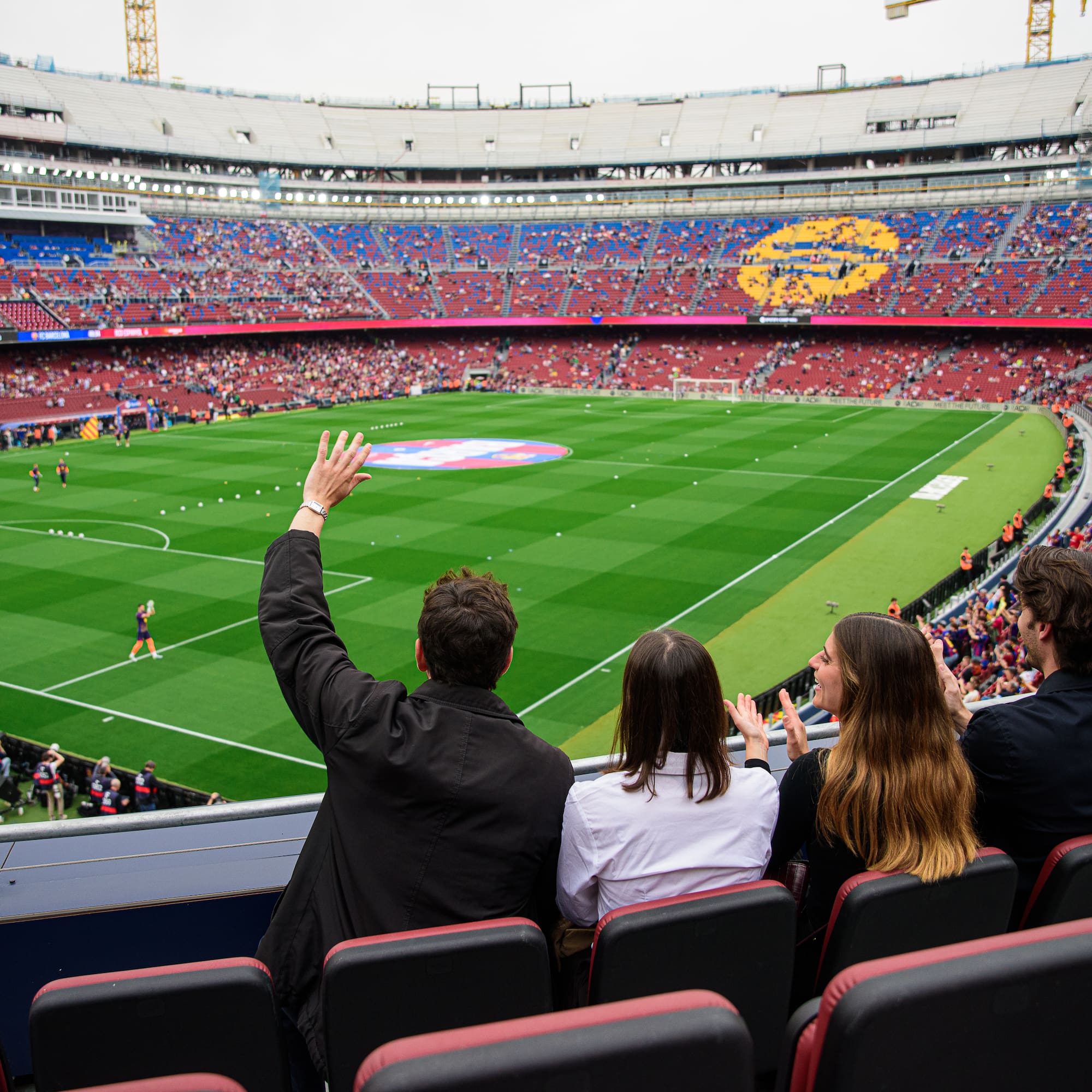 Four fans cheering in a stadium, watching a football match from seats.