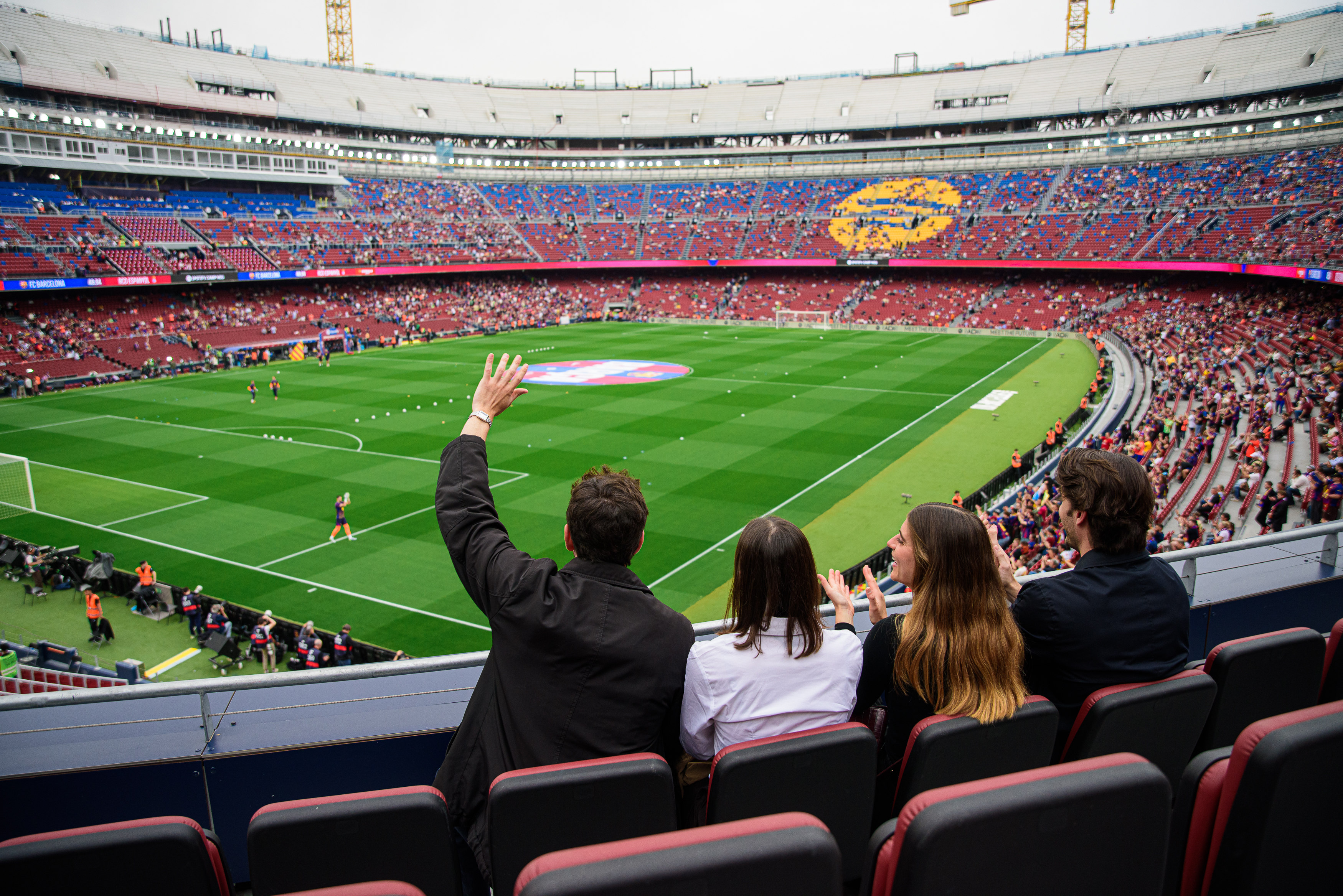 Four fans cheering in a stadium, watching a football match from seats.