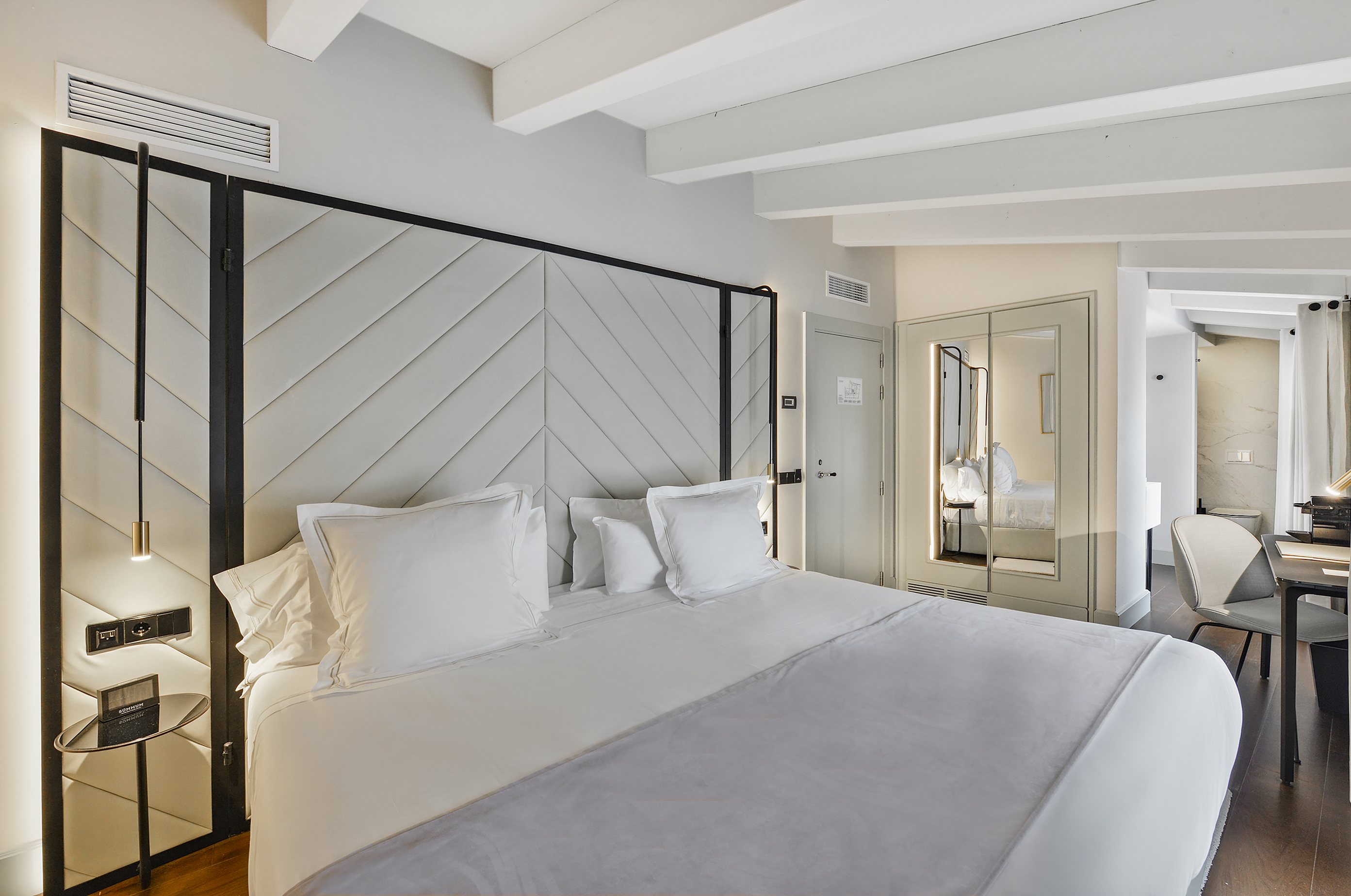 Modern hotel room with white bed, chevron headboard, and sleek interior design.