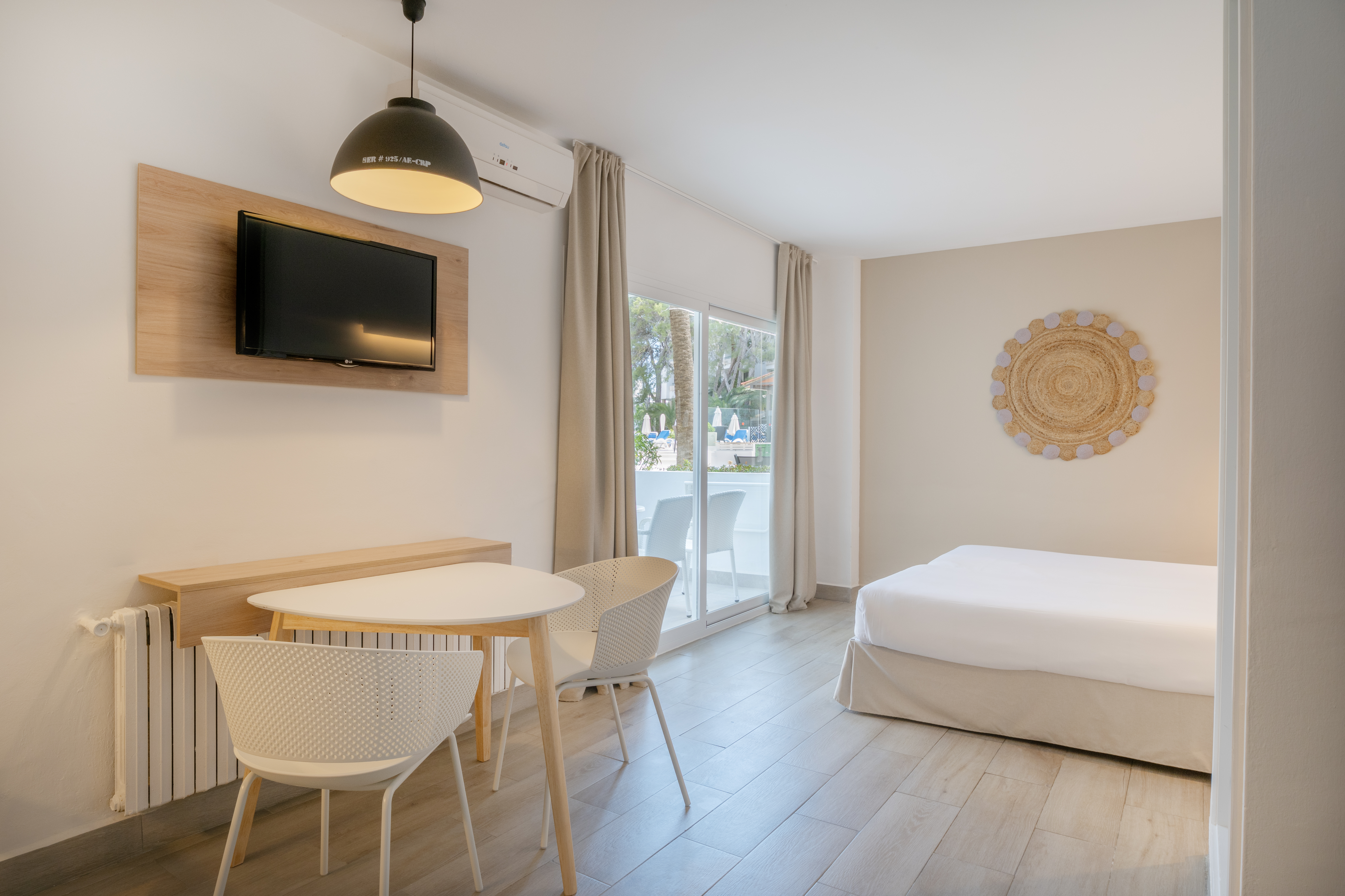 Bright modern hotel room with bed, dining area, TV, and balcony.