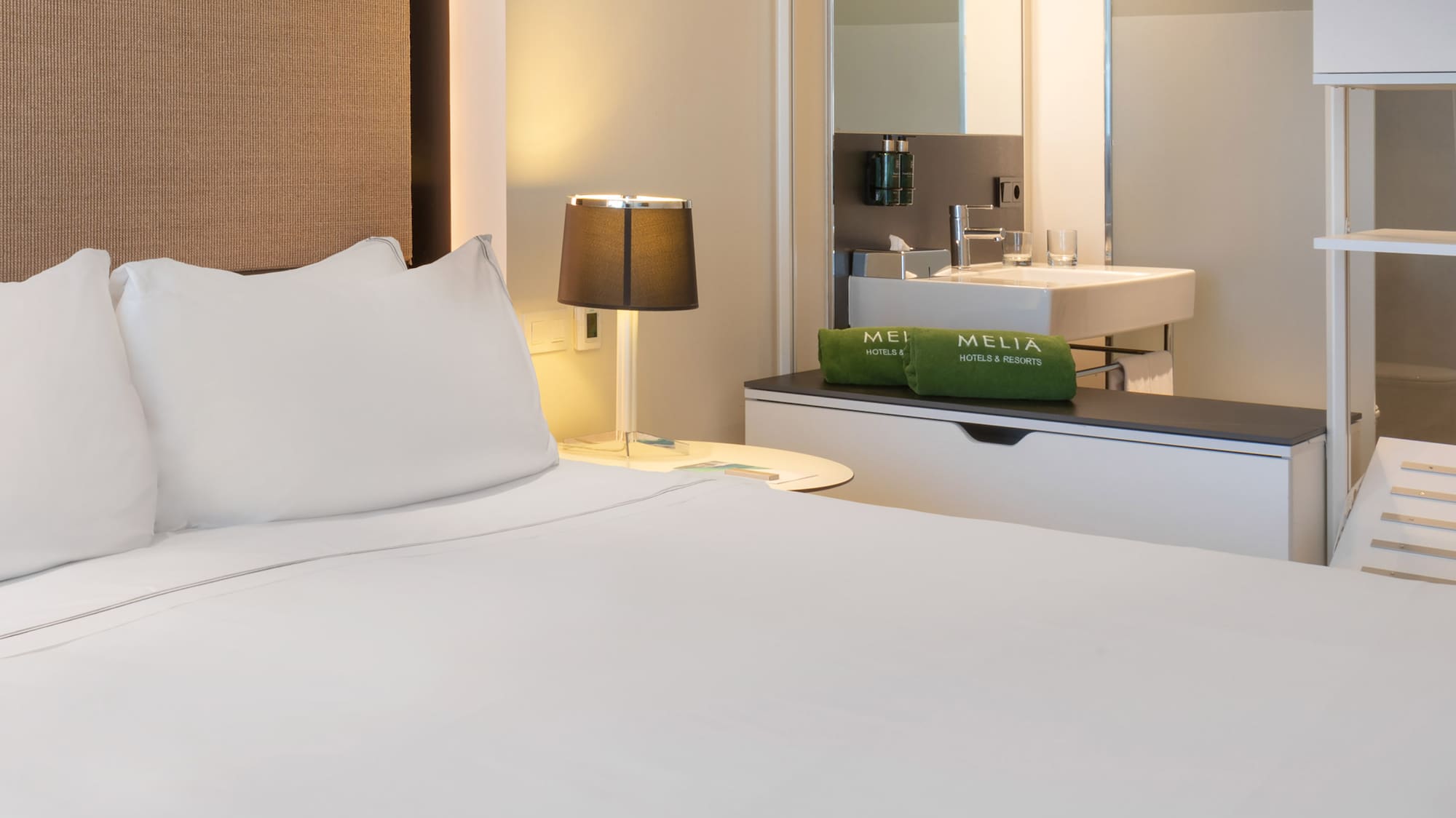 a bed with white sheets and a sink in a room