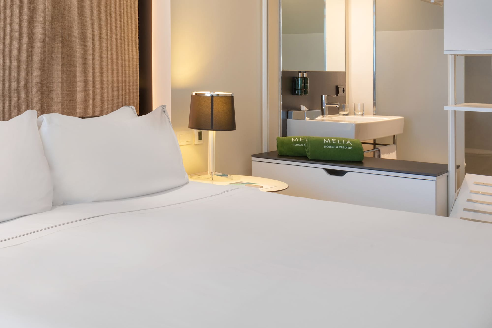 a bed with white sheets and a sink in a room