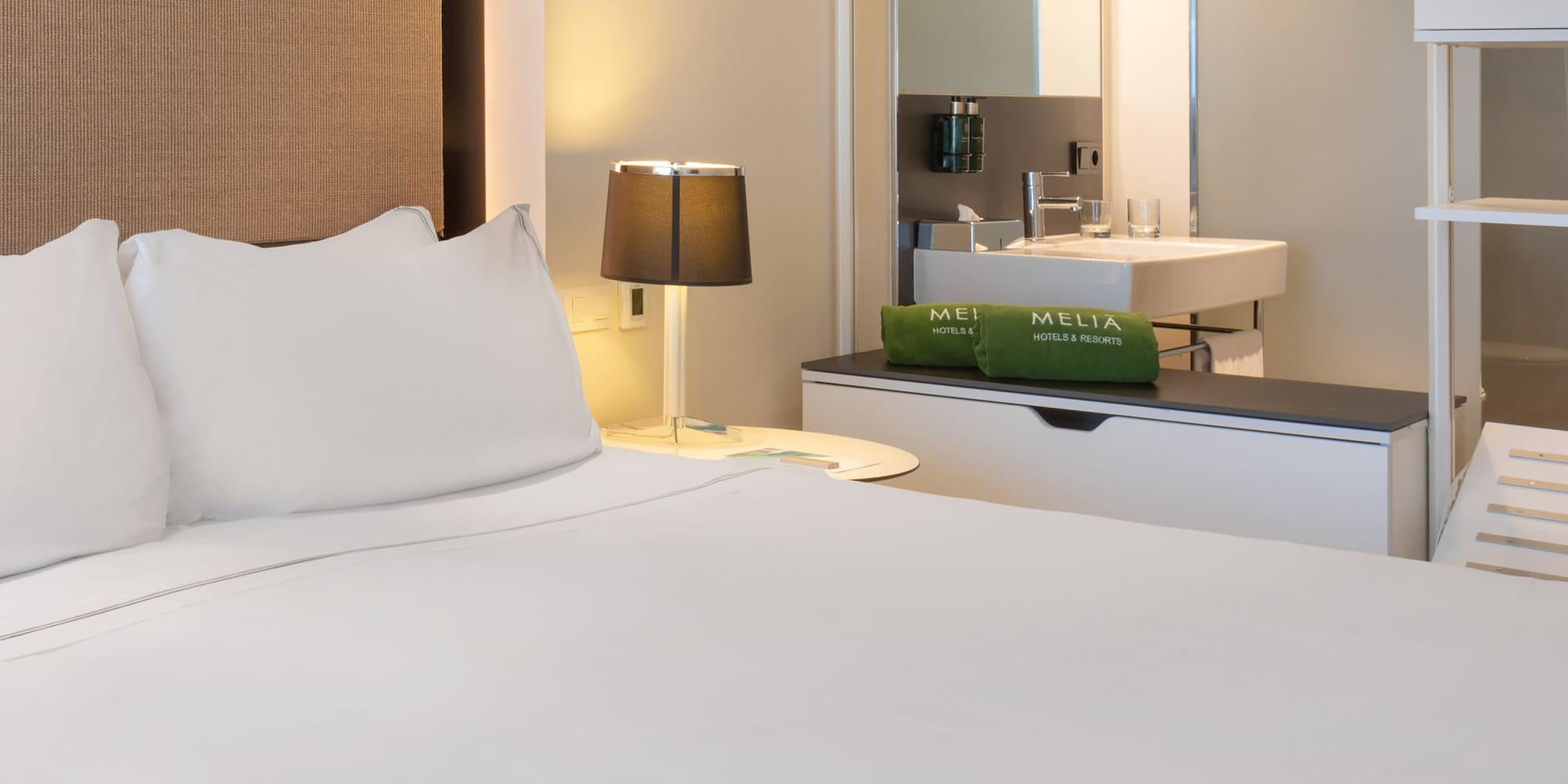 a bed with white sheets and a sink in a room