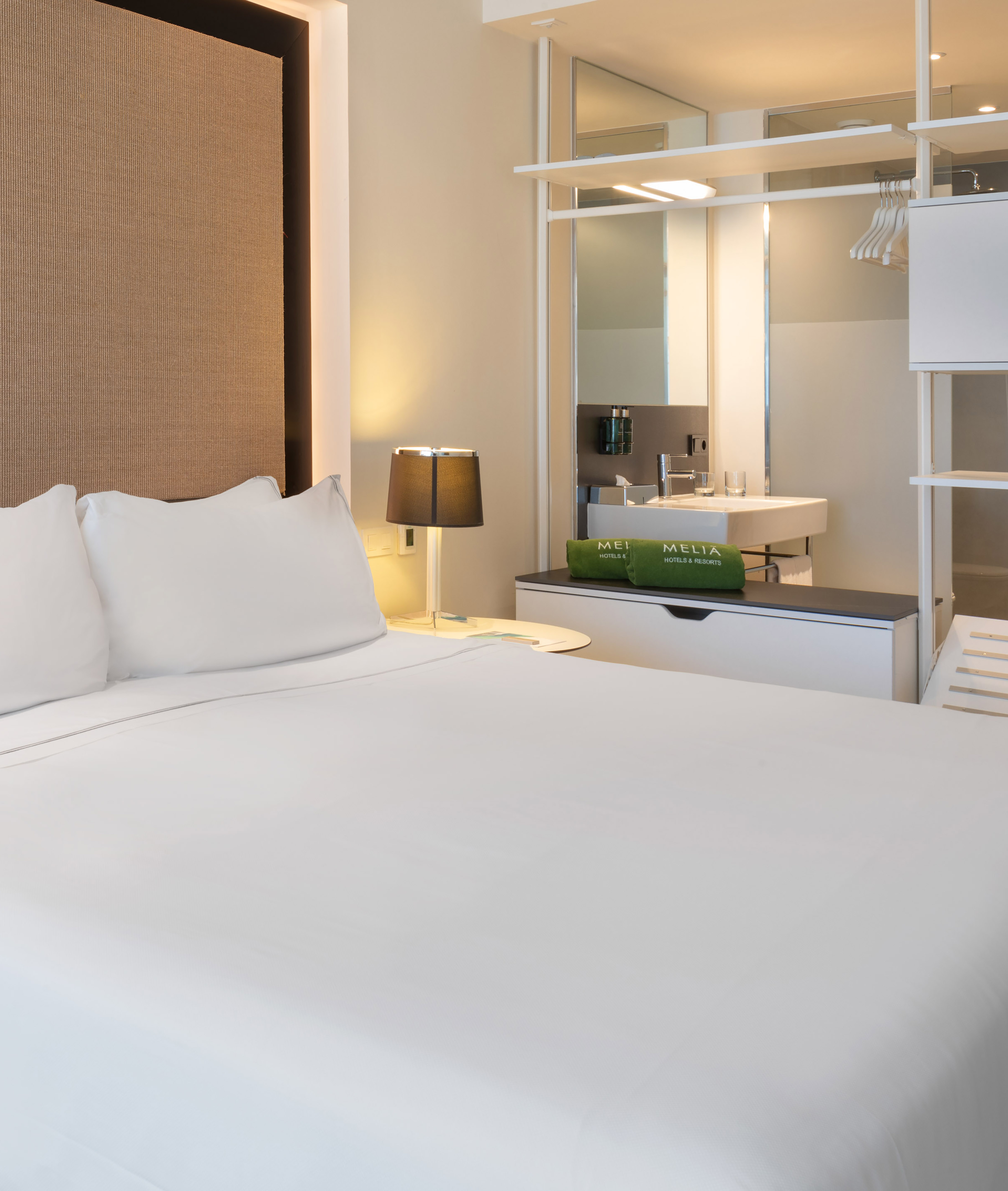 Modern Meliá hotel room with white bed, headboard, lamp, and open vanity.