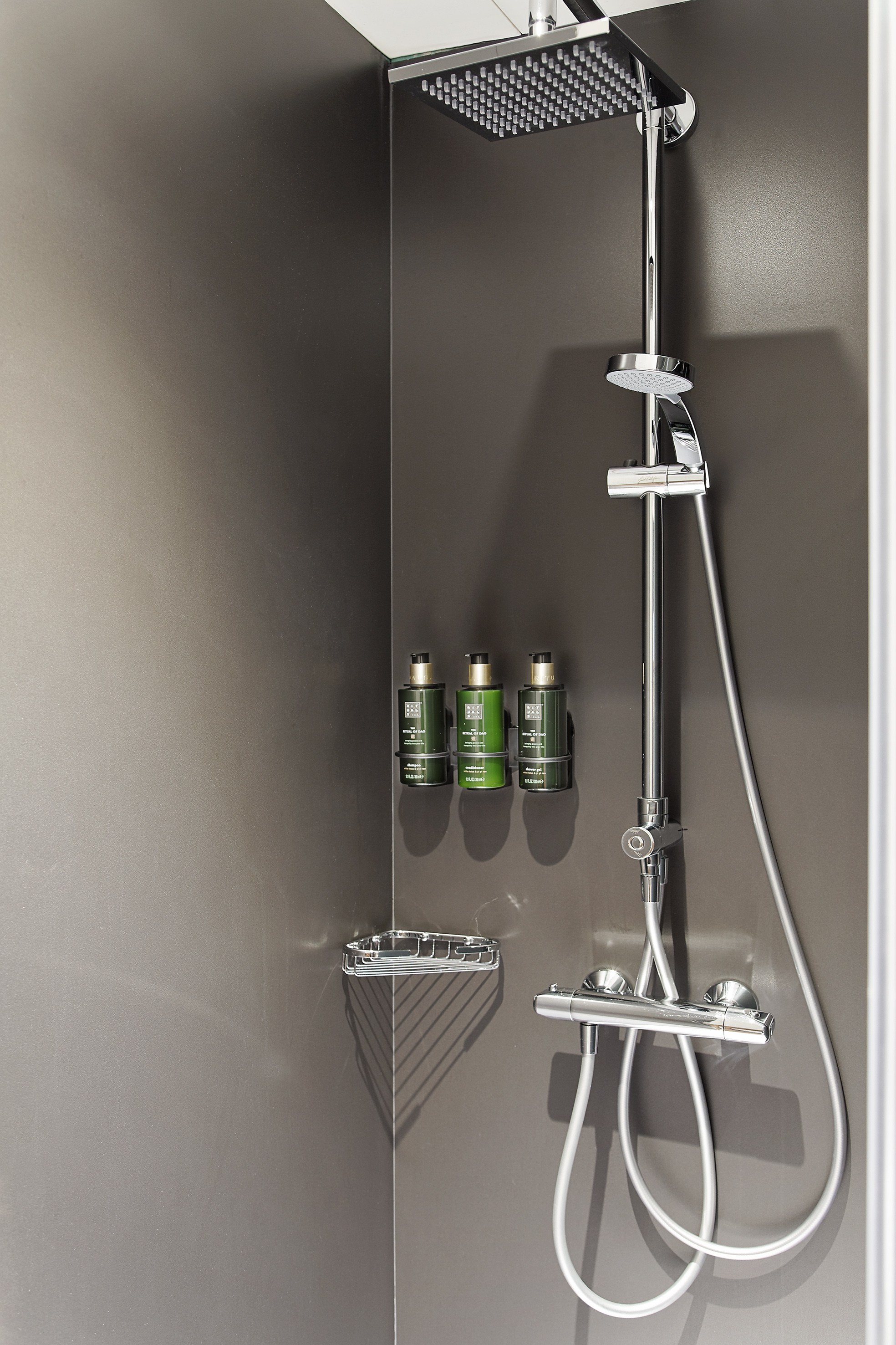 Chrome hotel shower with rain head, handheld, and Rituals bath products.