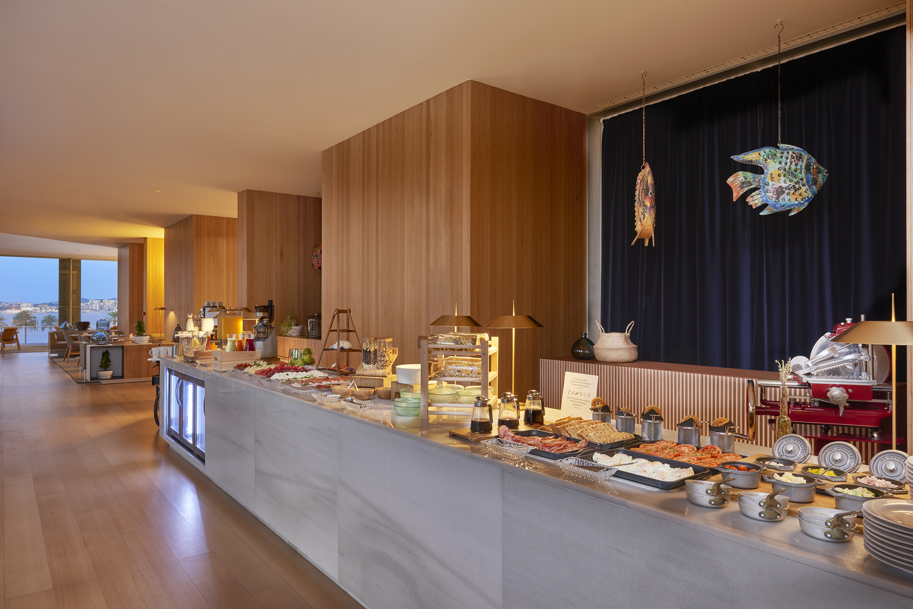 Modern breakfast buffet in hotel dining room with a scenic coastal view.