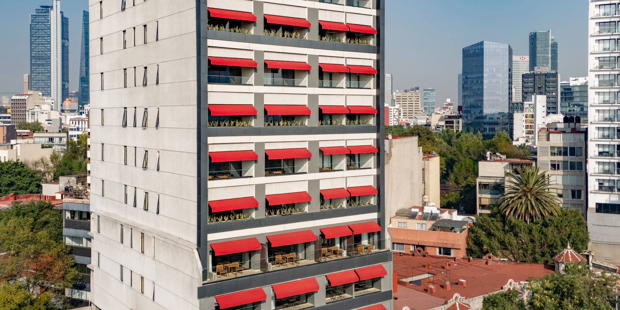 Modern grey building with bright red awnings over balconies, urban view.