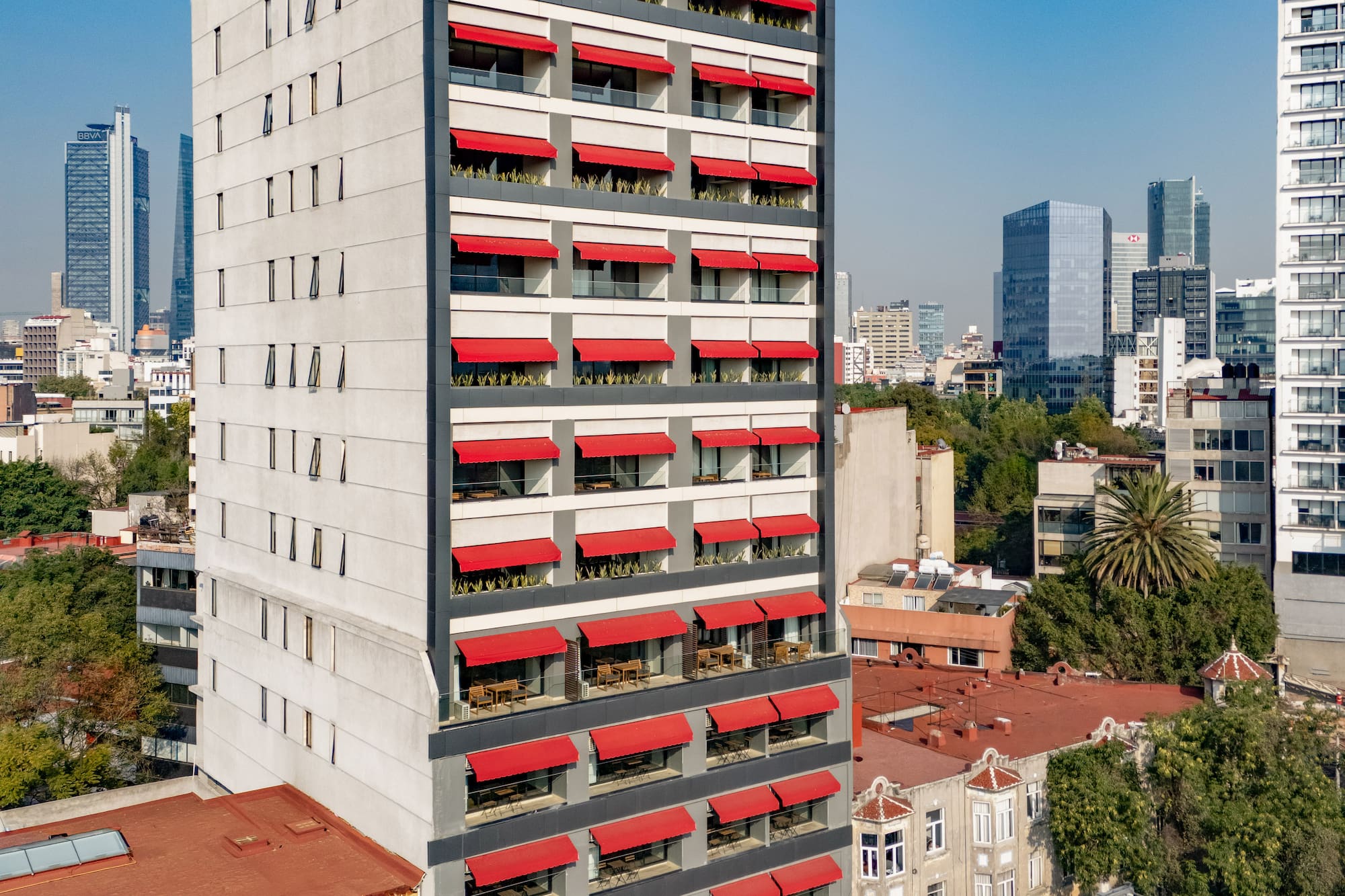 Modern grey building with bright red awnings over balconies, urban view.