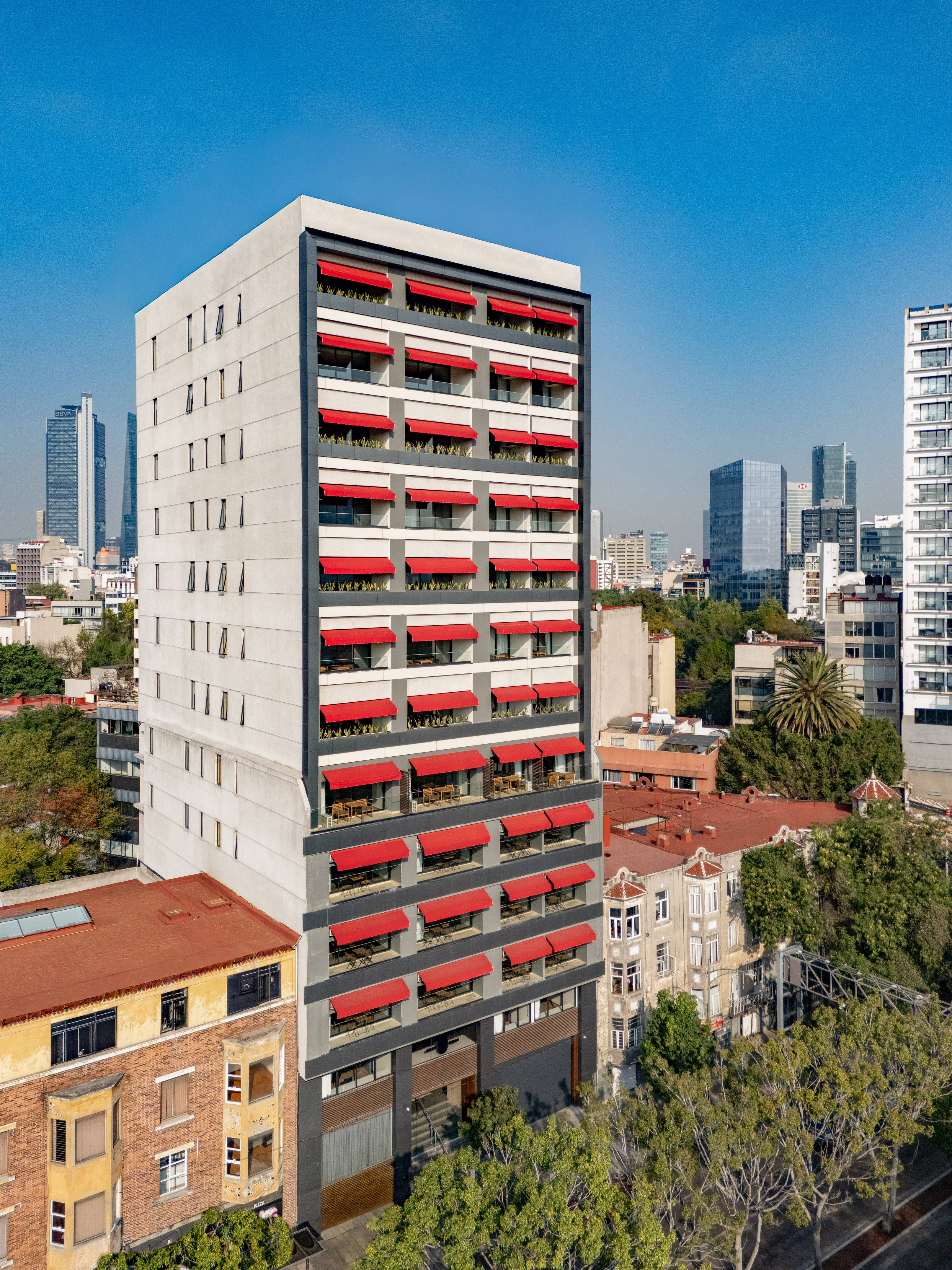 Modern grey building with bright red awnings over balconies, urban view.