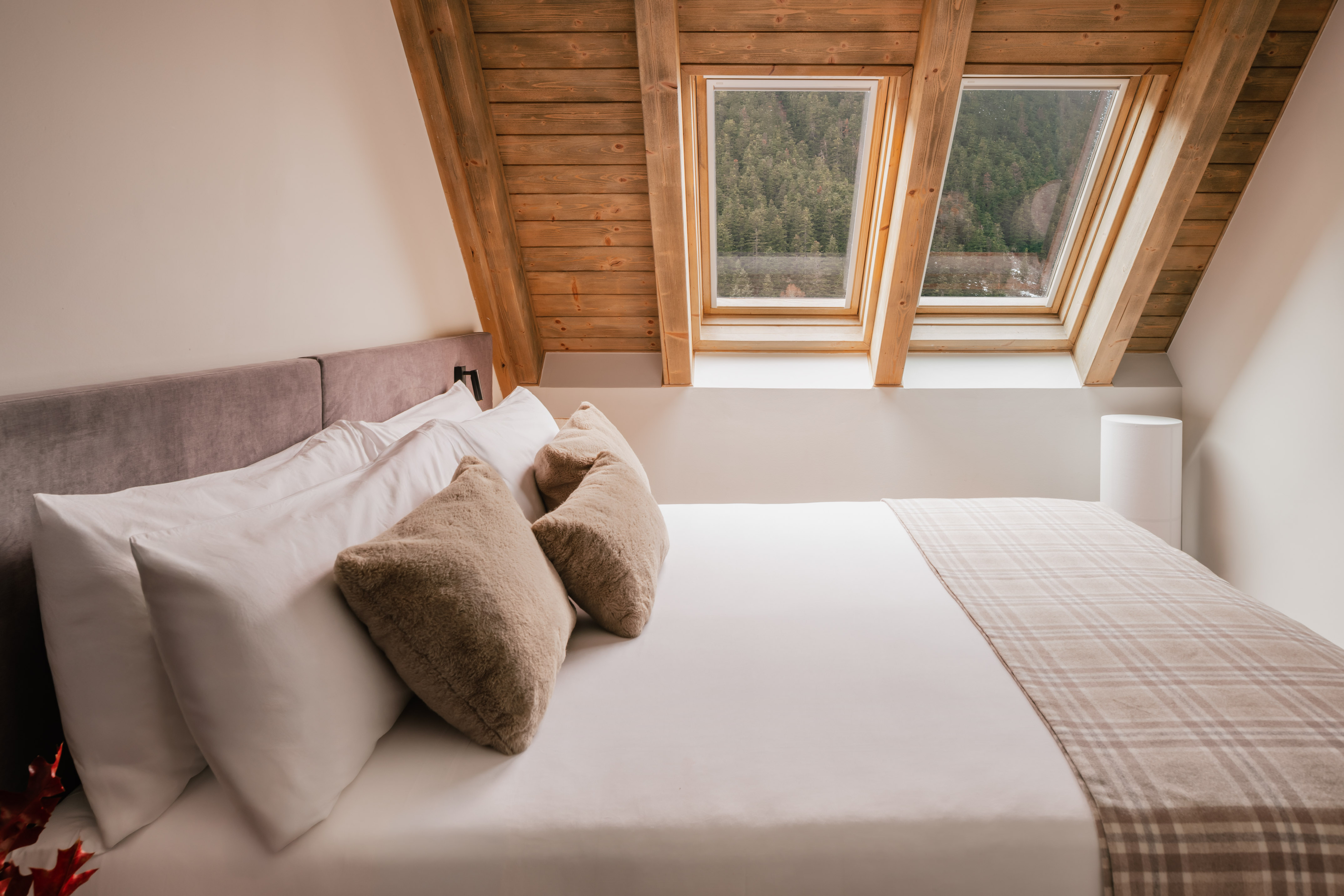 Cozy hotel bedroom with wooden beams, skylights, and mountain forest view.