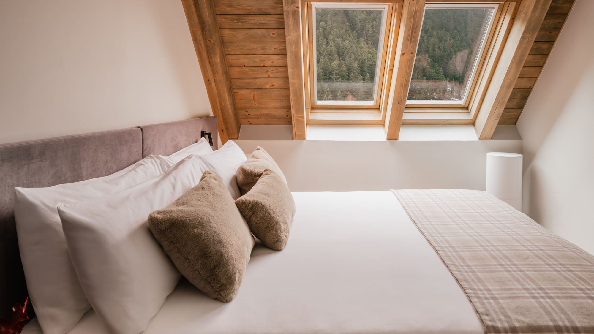Cozy hotel bedroom with wooden beams, skylights, and mountain forest view.
