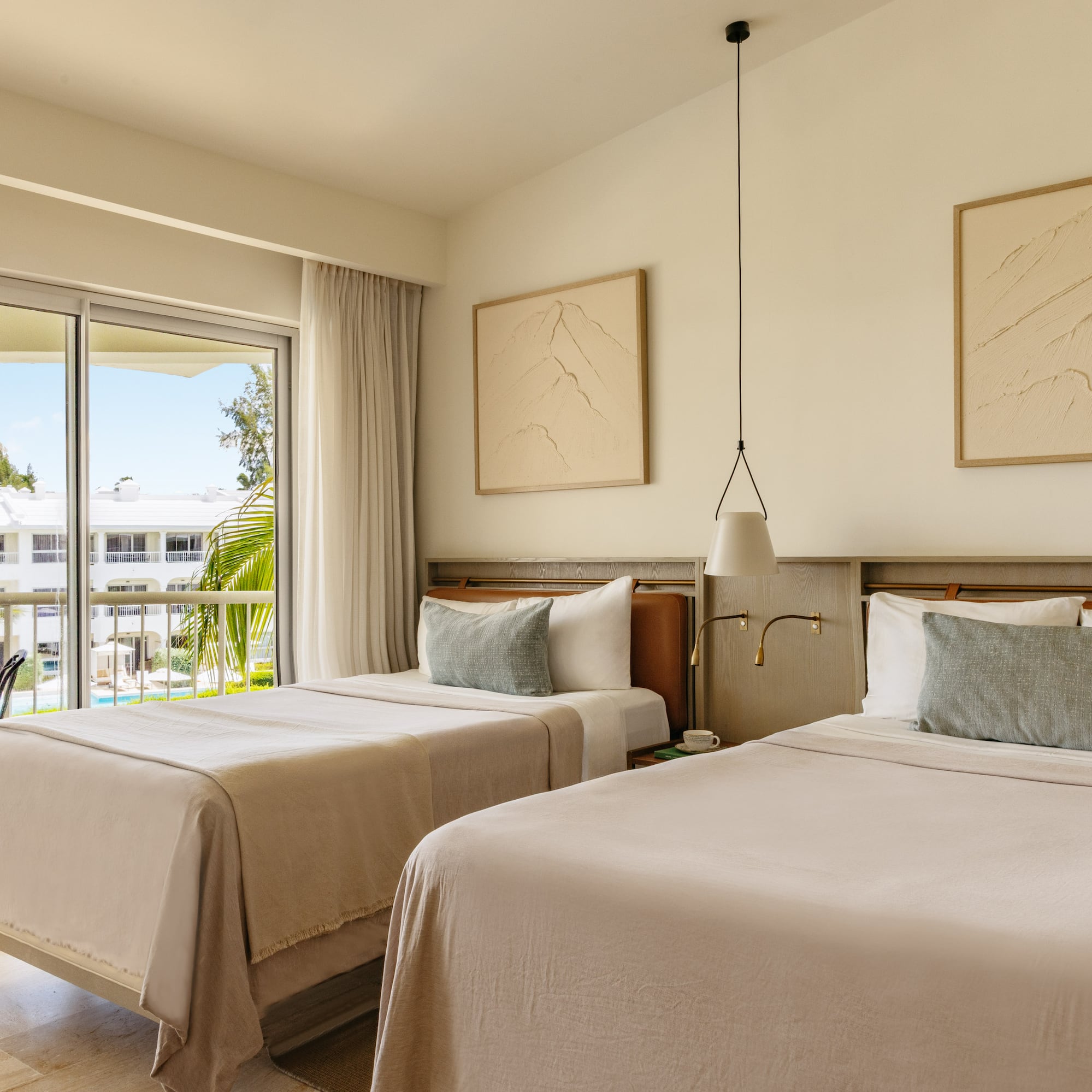 Modern resort room with twin beds, balcony, and tropical palm tree view.