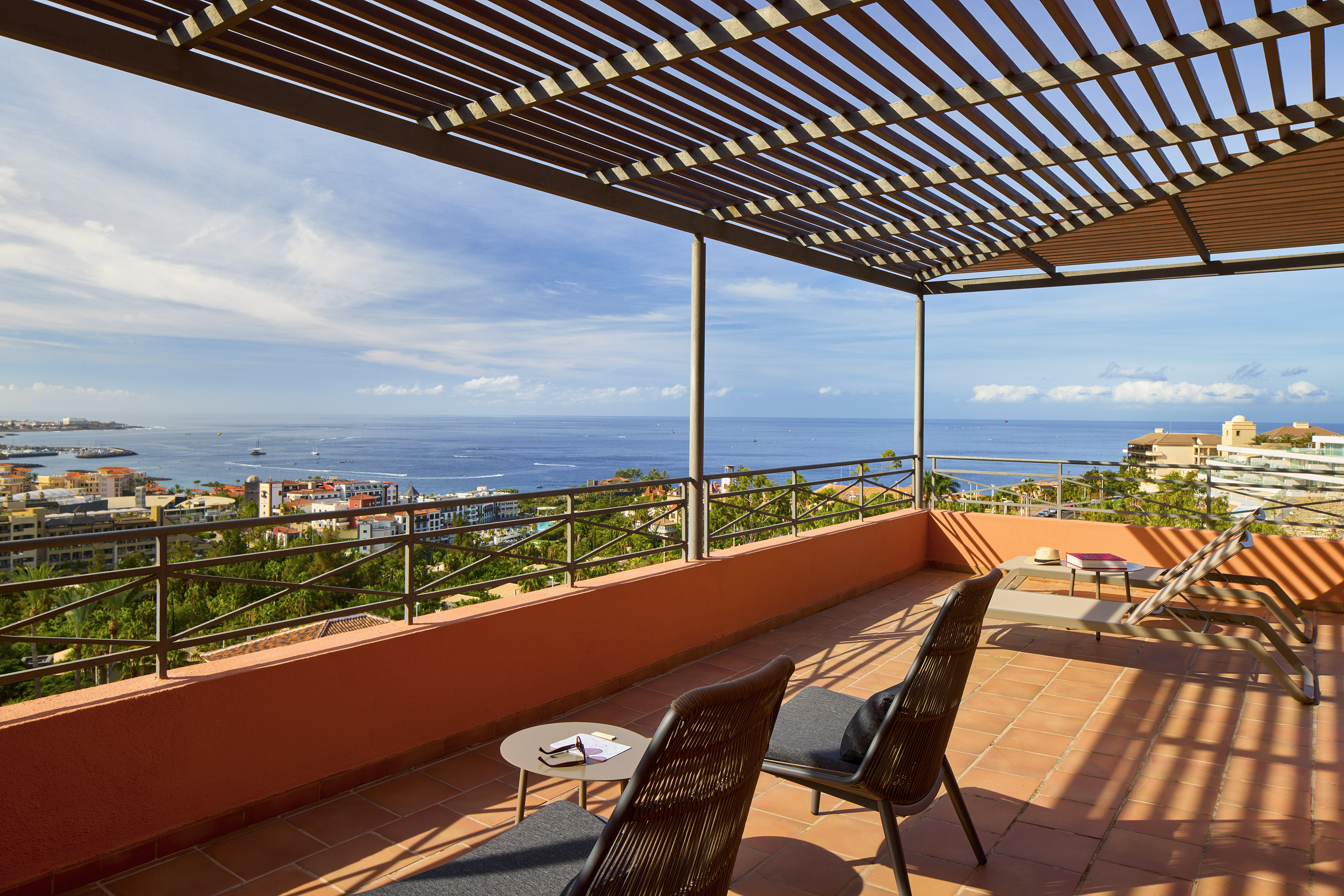 Ocean view terrace with coastal town, wooden pergola, and sun loungers.