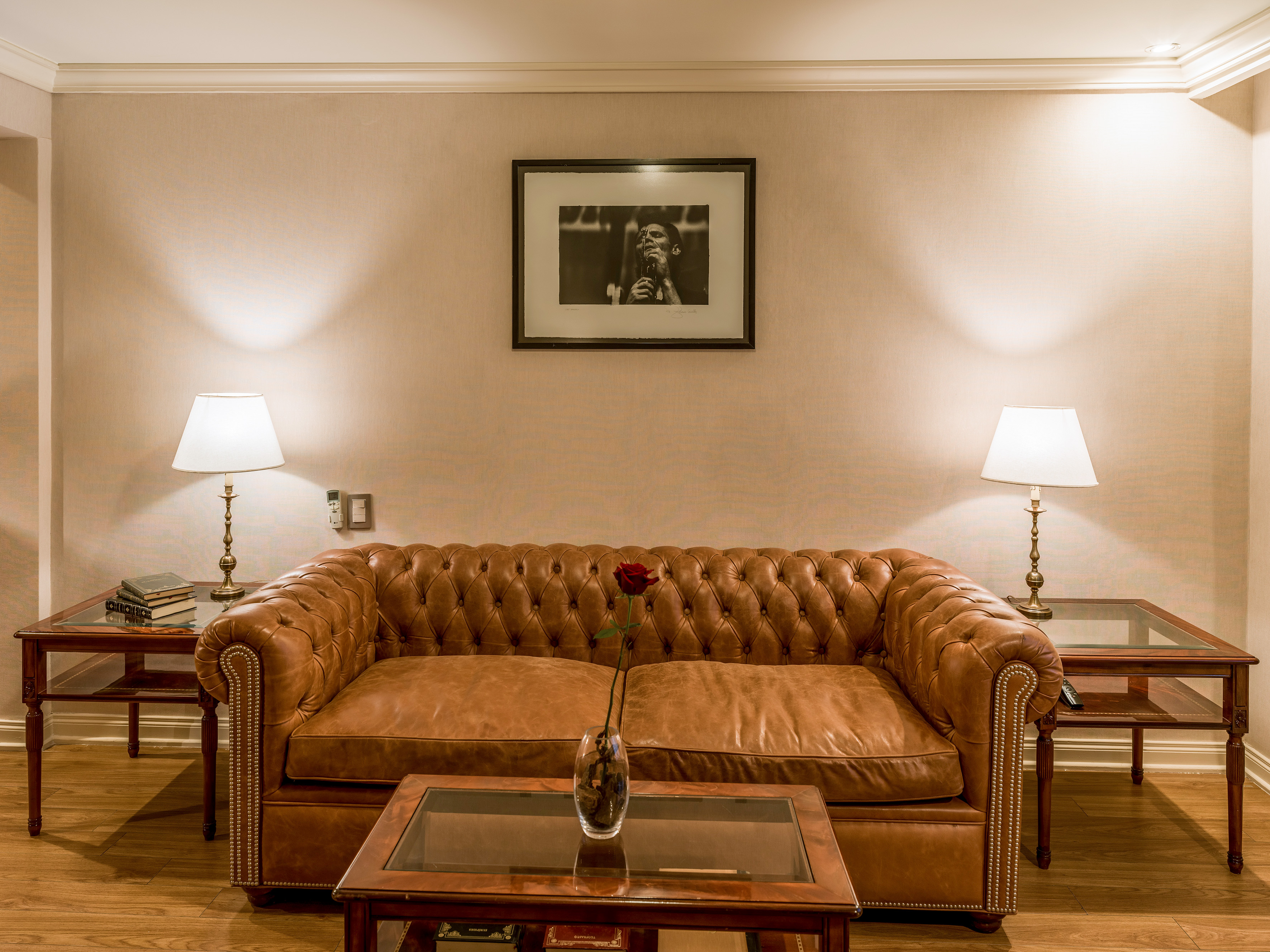 Brown leather Chesterfield sofa, lamps, and framed art in an elegant room.
