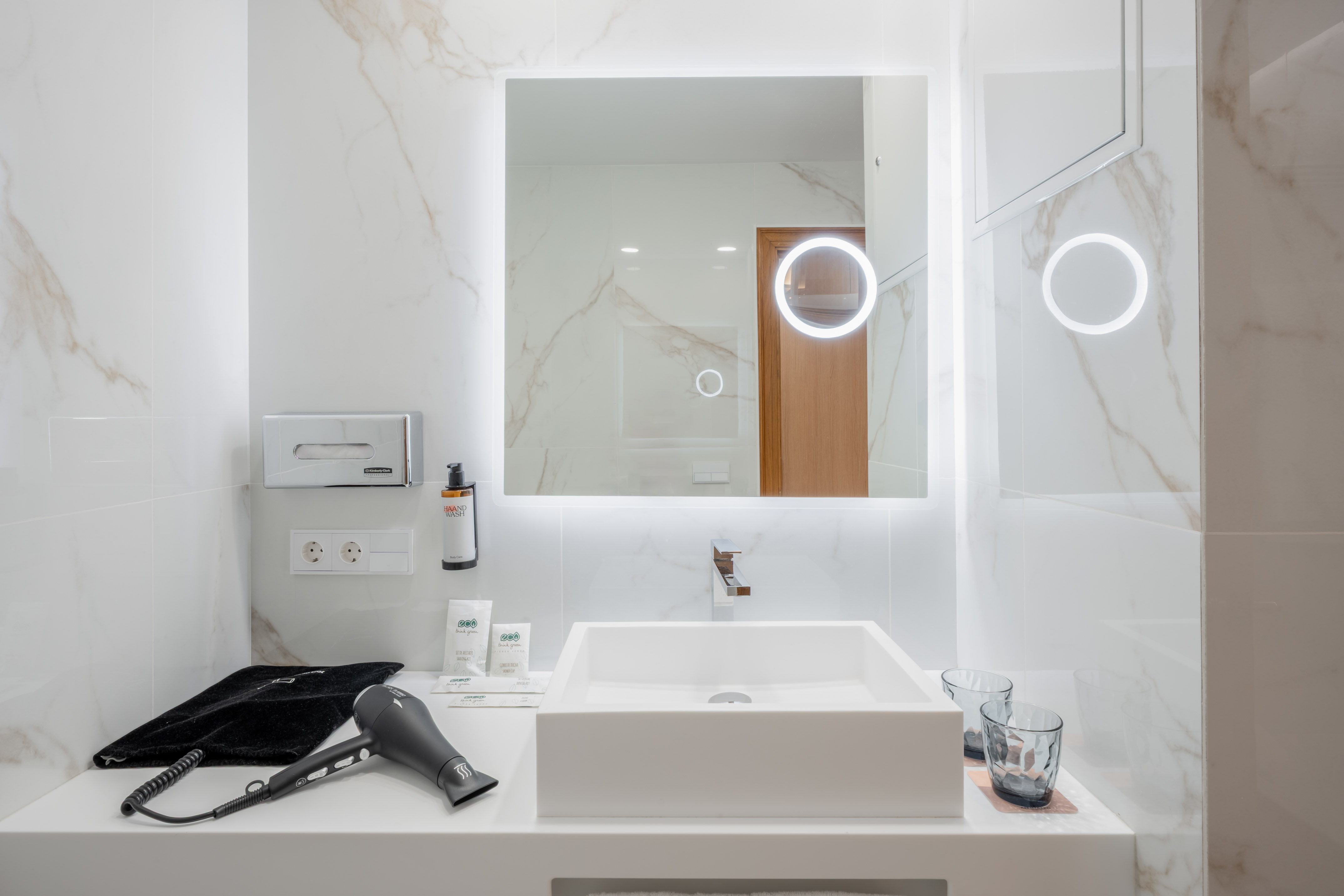 Modern hotel bathroom vanity with backlit mirror, square sink, and marble walls.