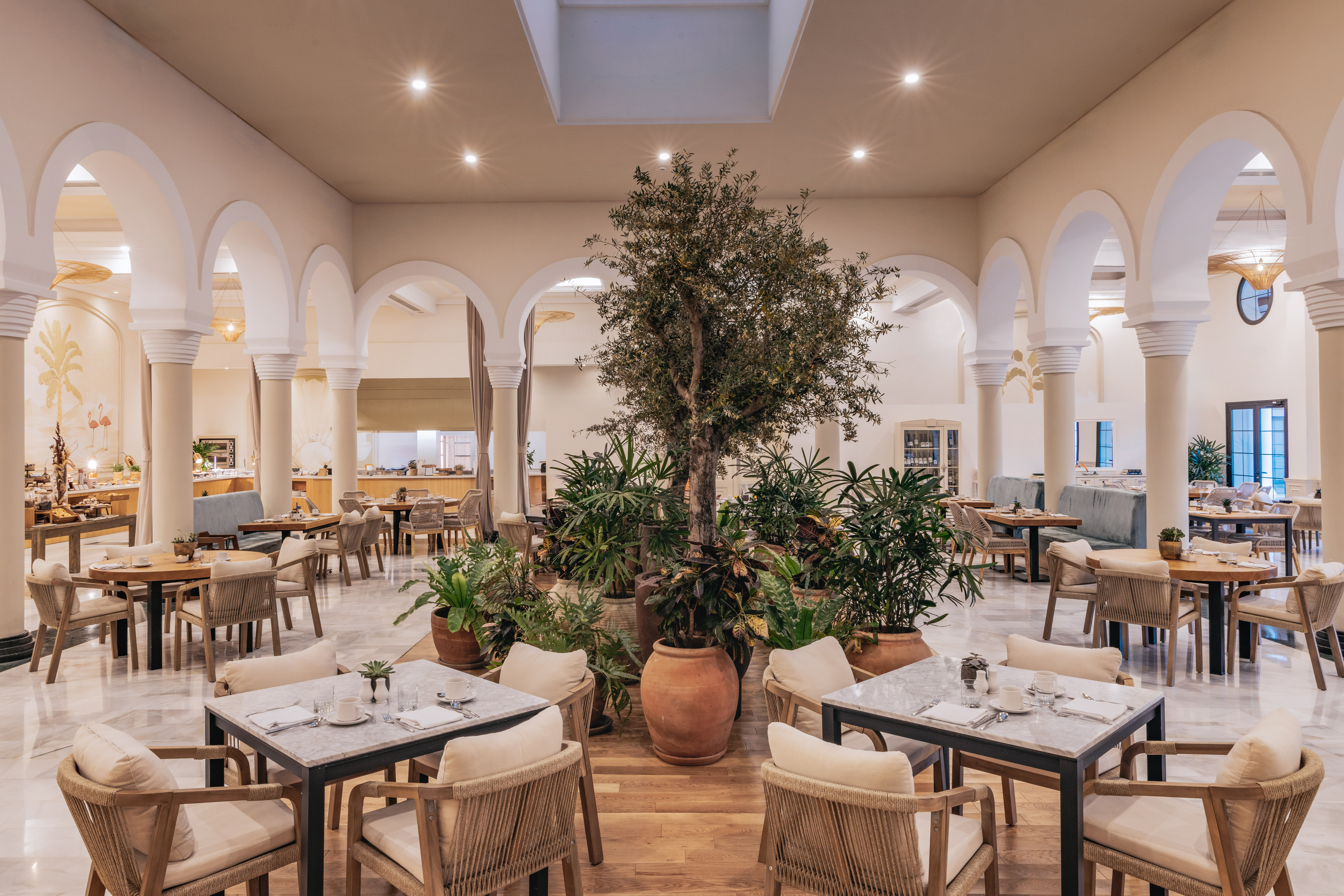 Elegant resort restaurant with arches, central tree, and dining tables.