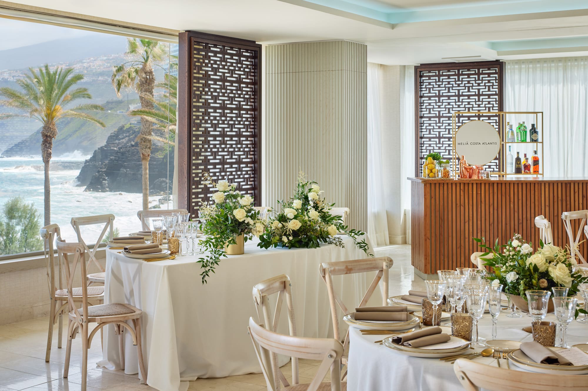 Meliá Costa Atlantis dining, elegant tables, ocean view, palm trees, white florals.