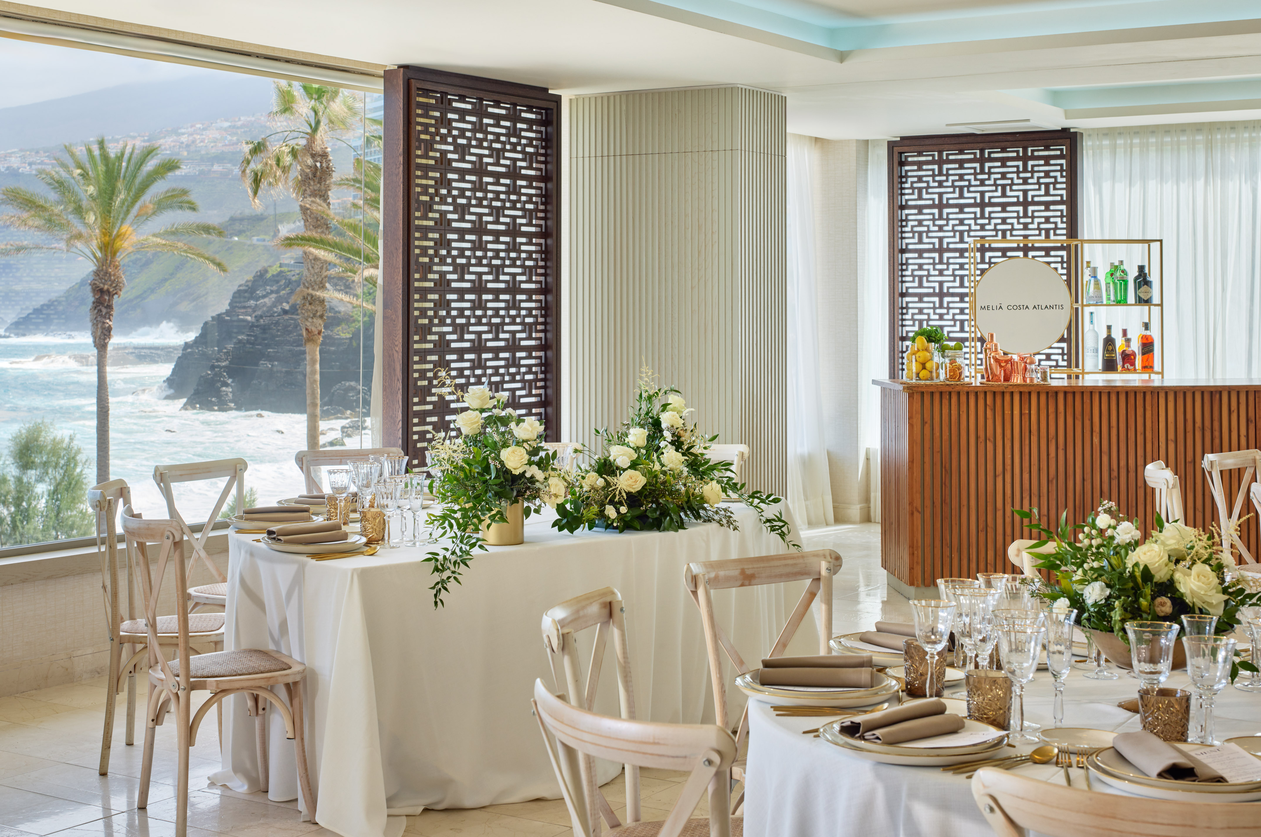 Meliá Costa Atlantis dining, elegant tables, ocean view, palm trees, white florals.