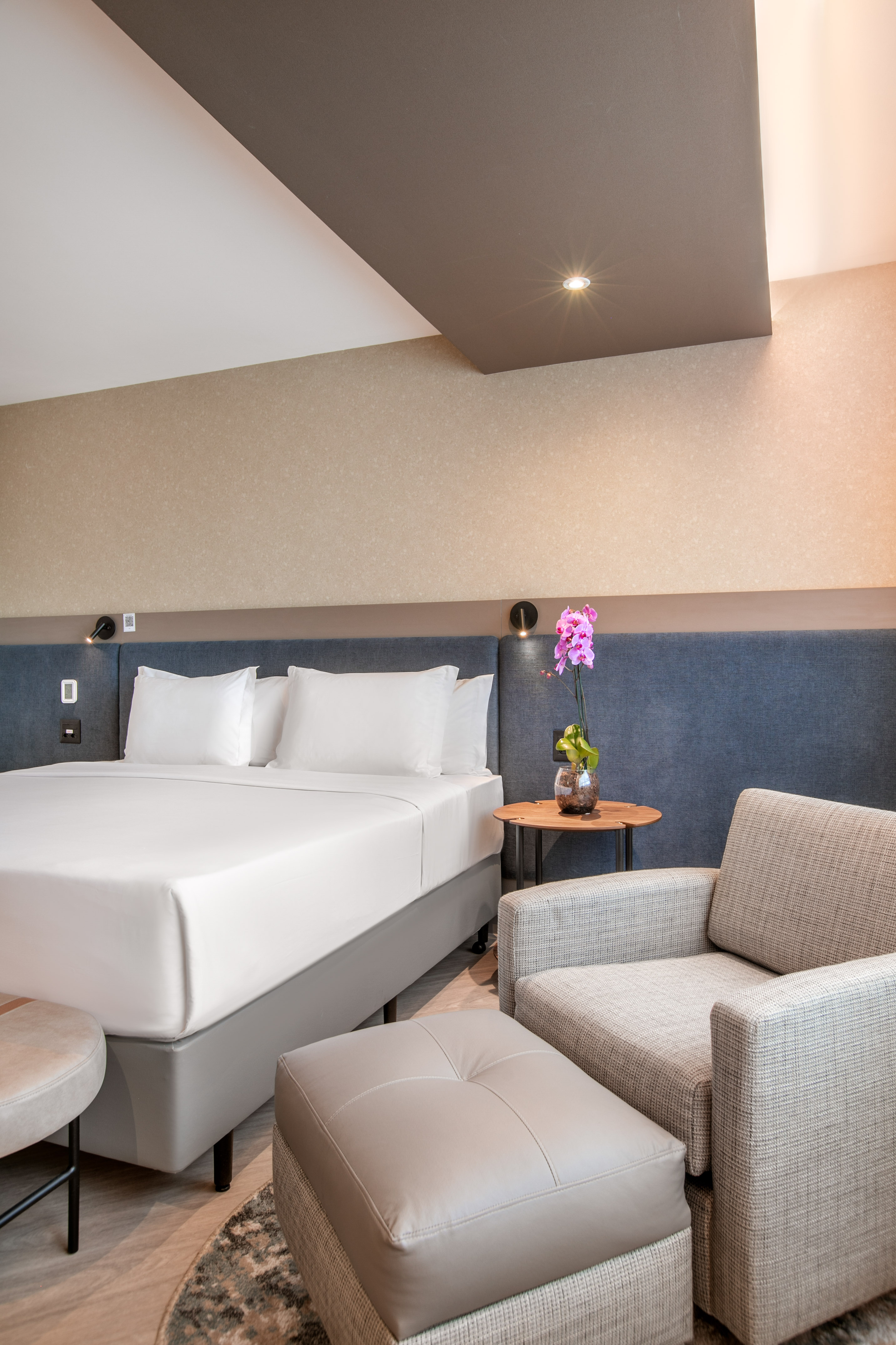 Contemporary hotel room with white bed, cozy armchair, and decorative orchid.